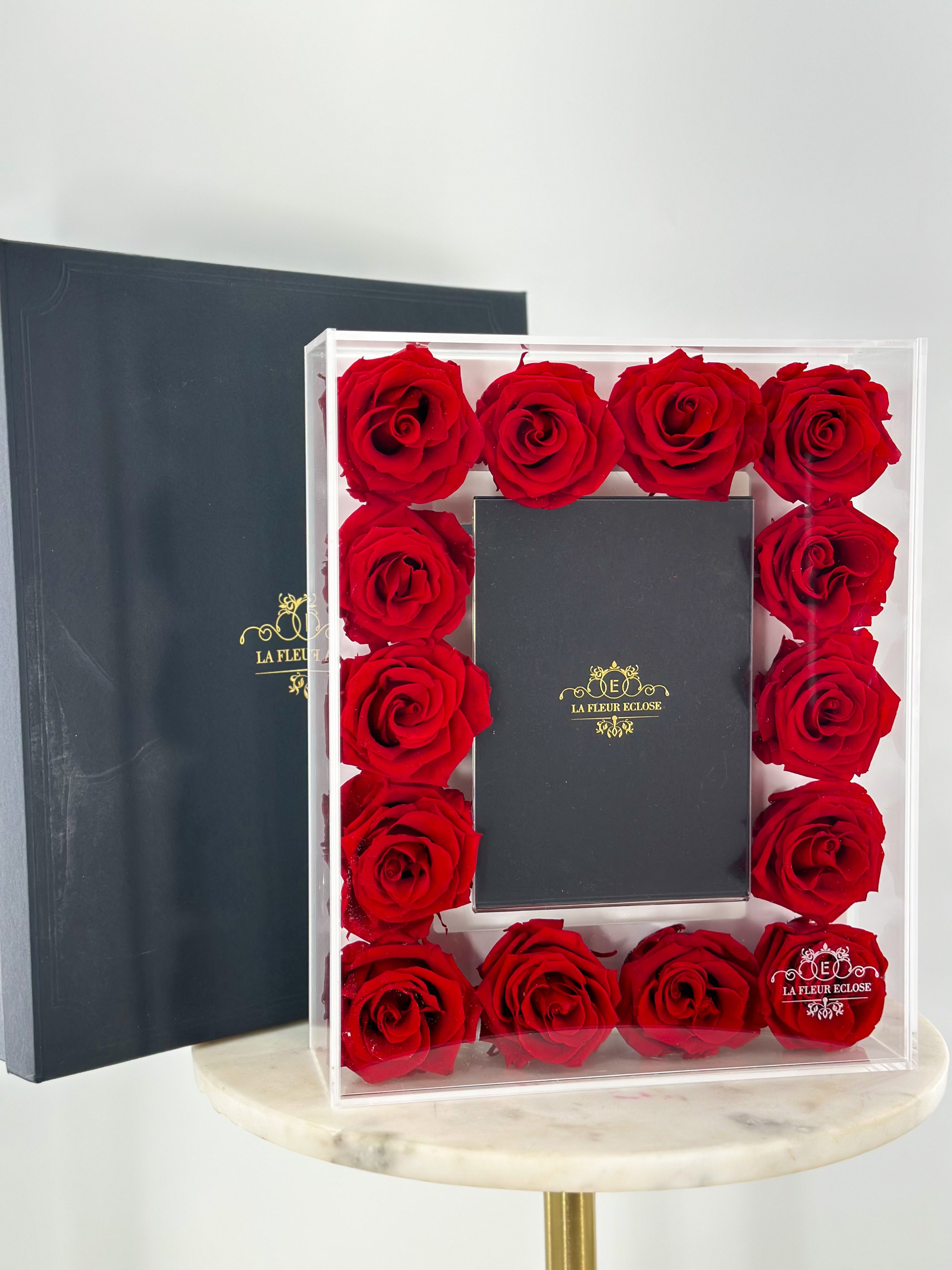 Red roses arranged in a clear box around a black gift box