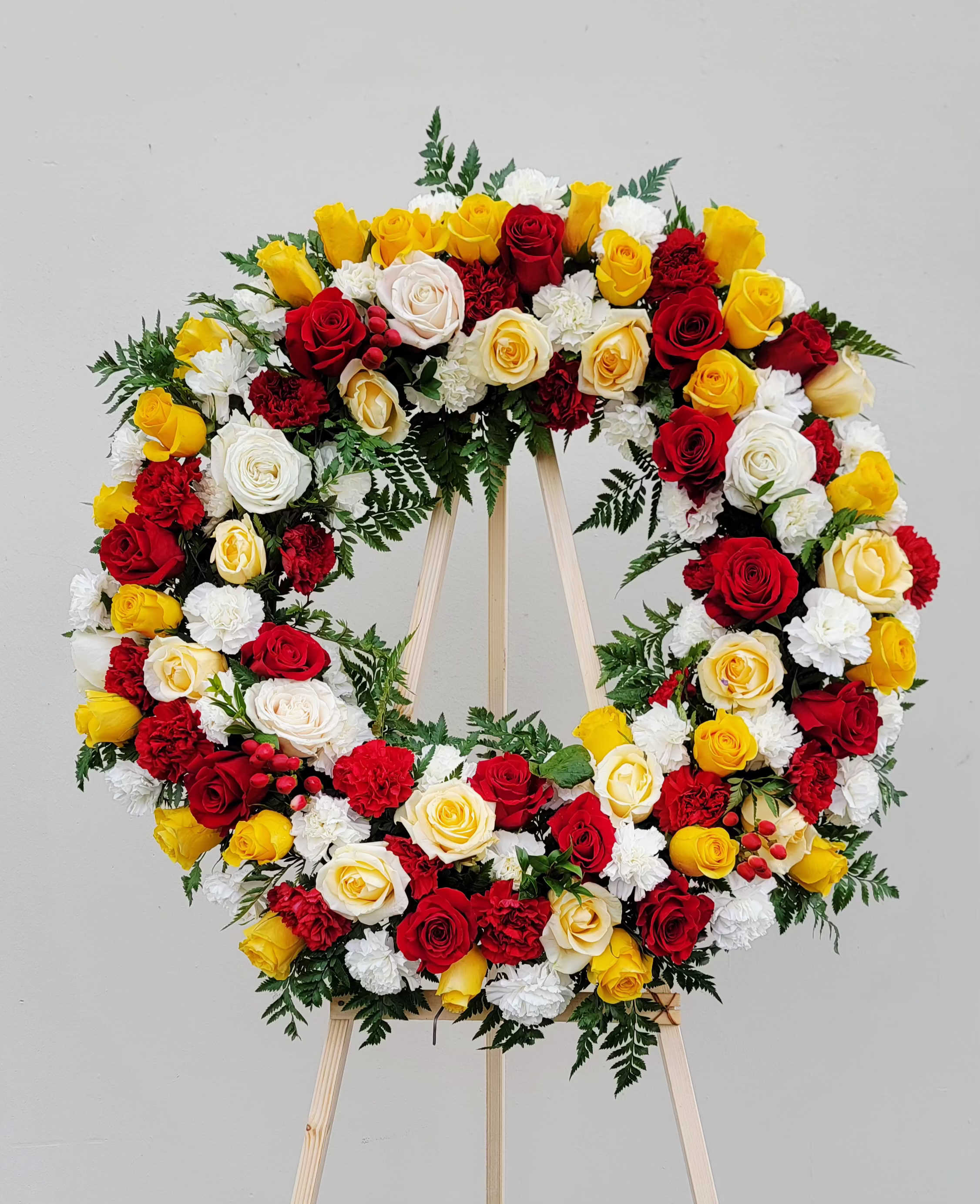 Circular wreath of red, yellow, and white roses on a wooden easel