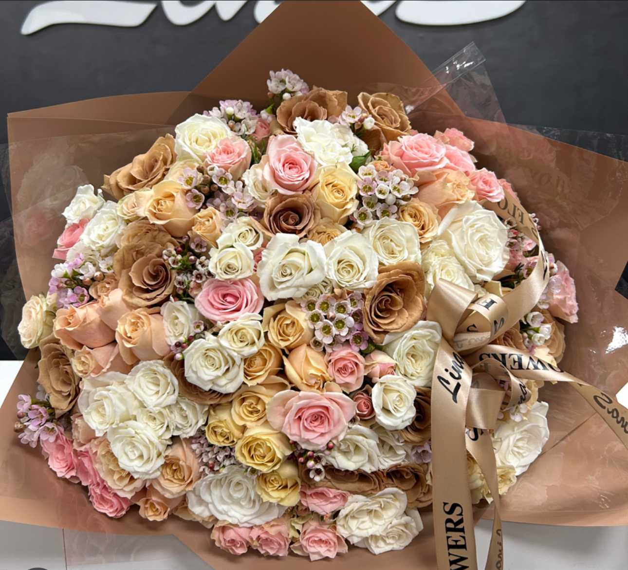 Large bouquet of pastel roses wrapped in brown paper with a satin ribbon