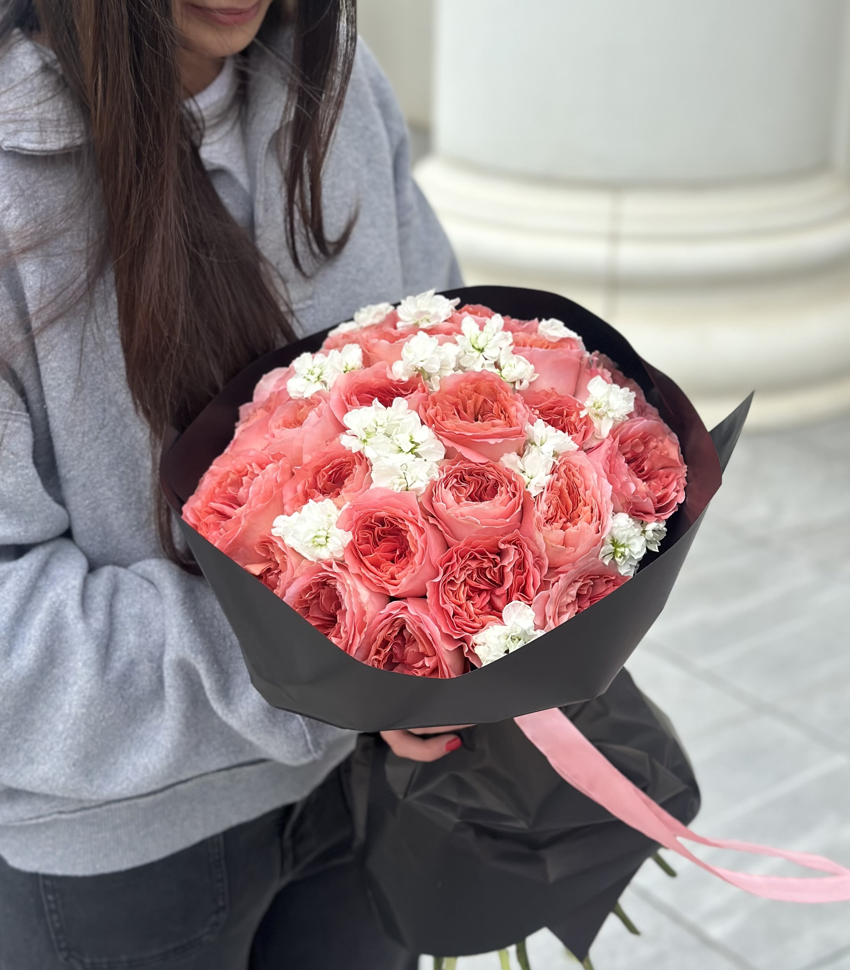 Bouquet of pink roses with small white flowers wrapped in black paper