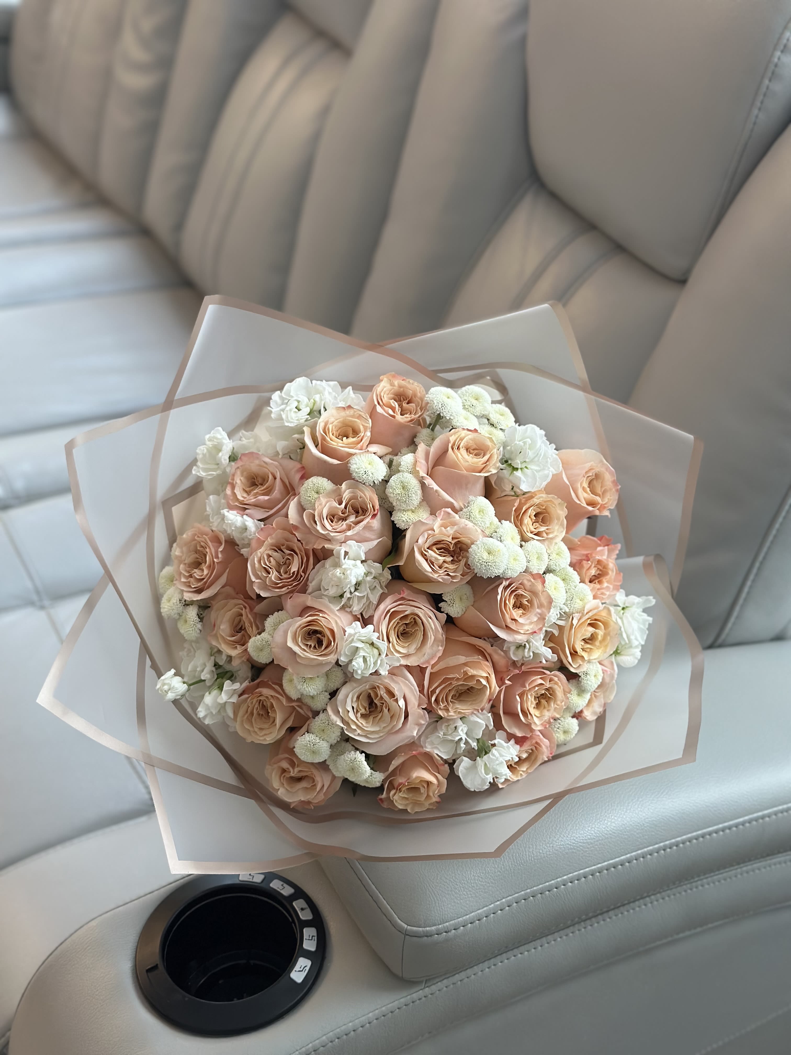 Bouquet of peach roses with white filler flowers wrapped in translucent paper