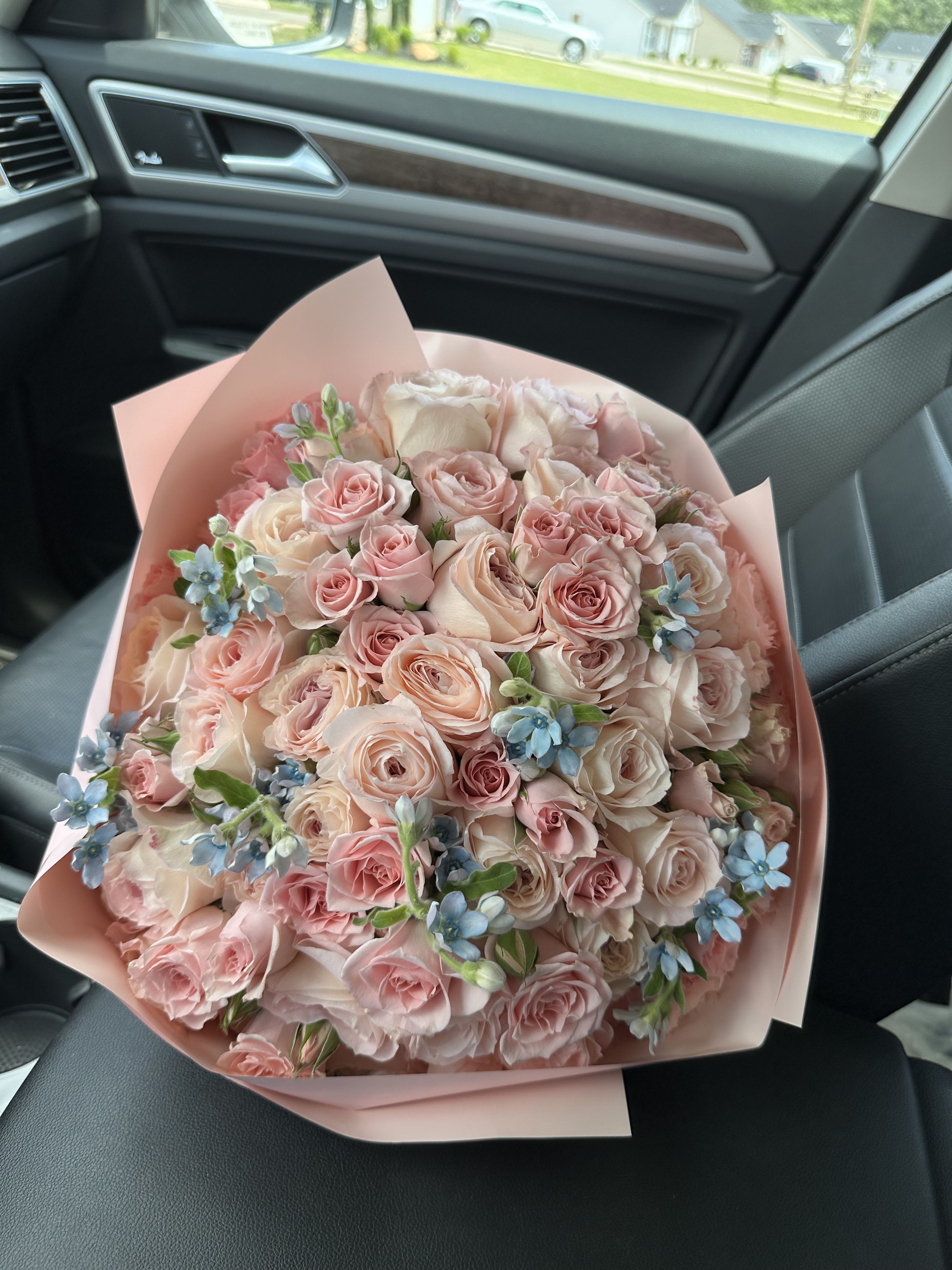 Bouquet of pale pink roses with small blue flowers wrapped in pink paper