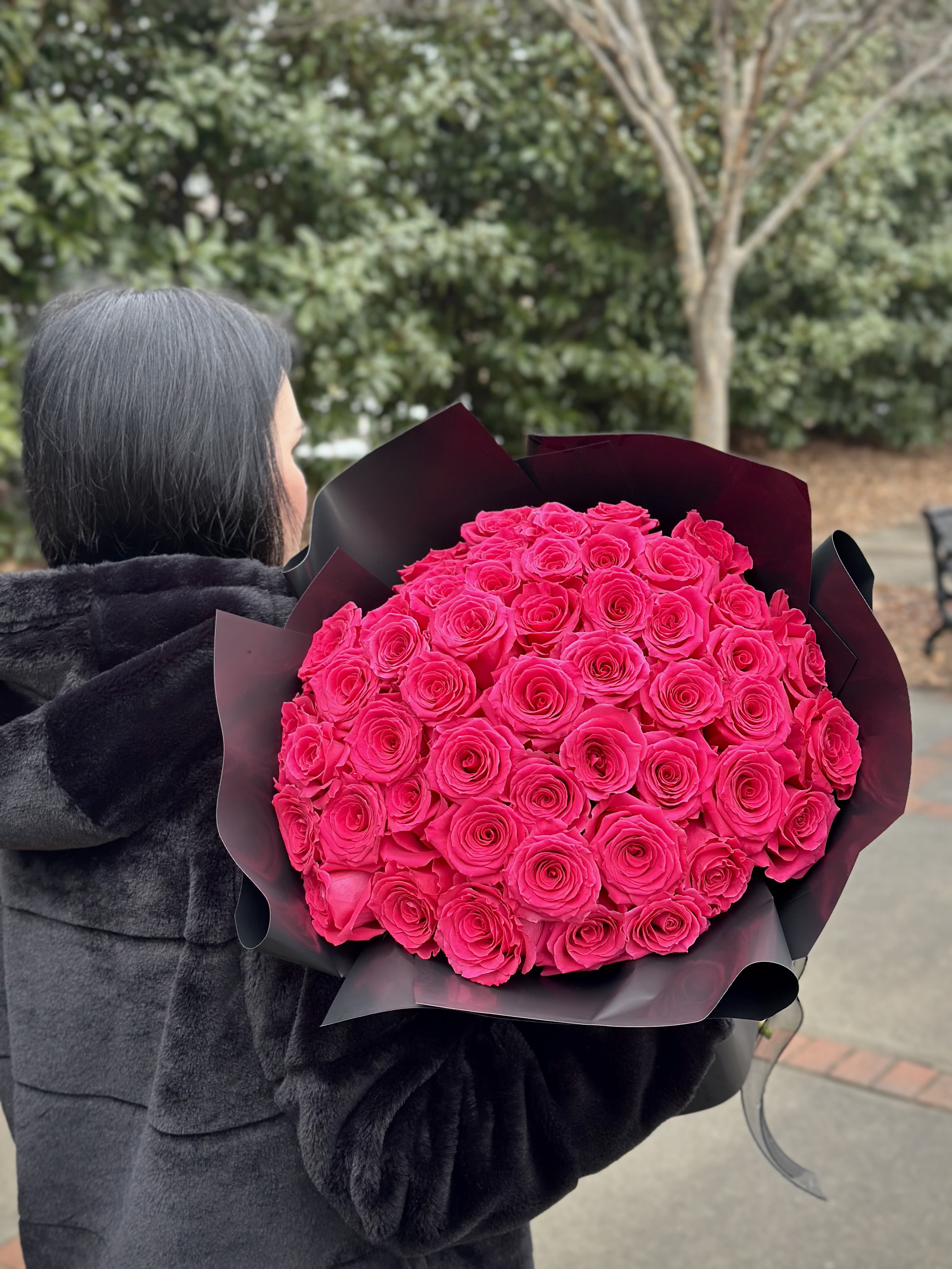 Person holding a large bouquet of bright pink roses wrapped in black paper