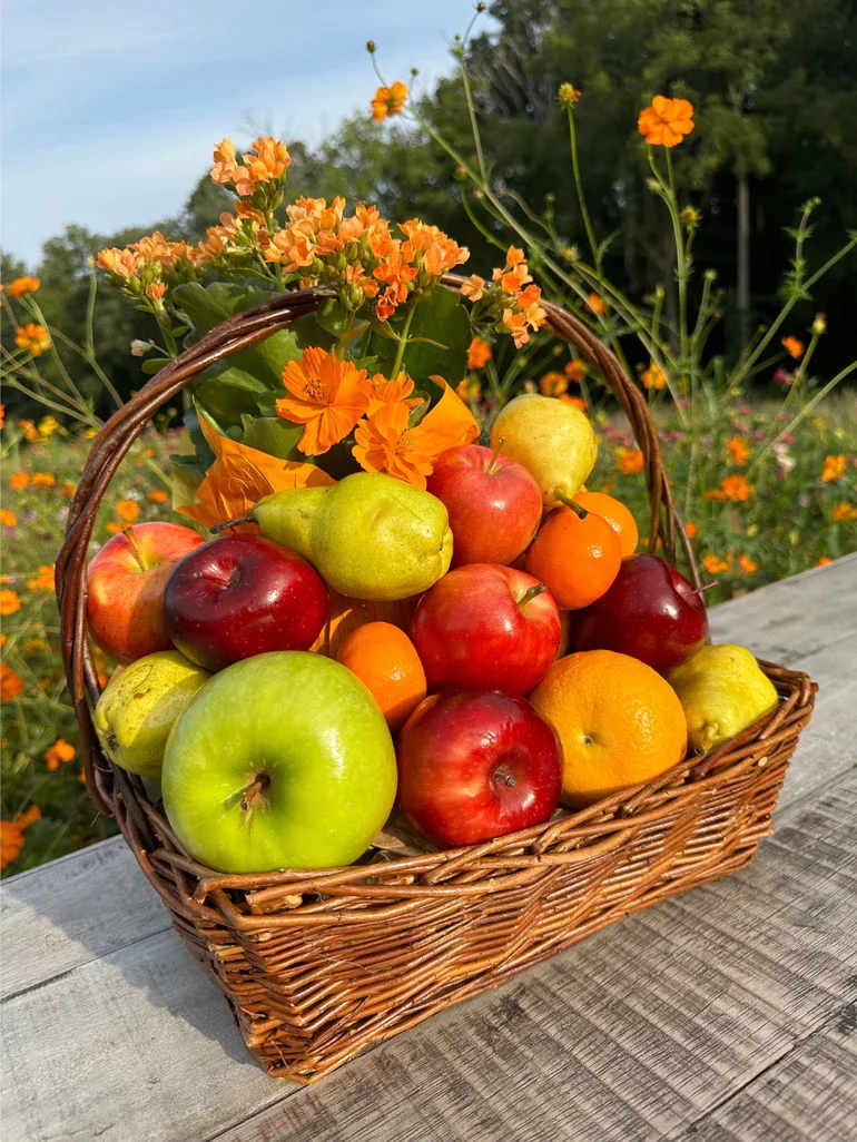 Wicker gift basket filled with assorted fresh fruit and topped with orange flowers