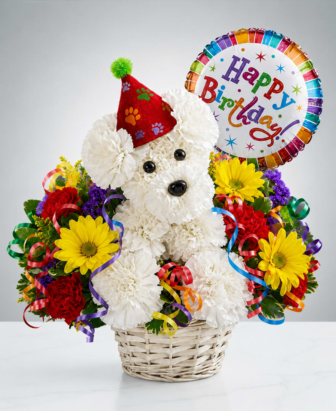 Birthday Celebration Pup - Birthday Wishes Puppy™  Celebrate someone's special day with this adorable handcrafted floral puppy! Expertly designed using fresh white carnations, this charming arrangement is accented with vibrant seasonal flowers, festive curly ribbons, a colorful birthday hat, and a cheerful Happy Birthday balloon. Arranged in a natural woven basket, it's a fun and memorable gift that is sure to bring smiles to recipients of all ages.