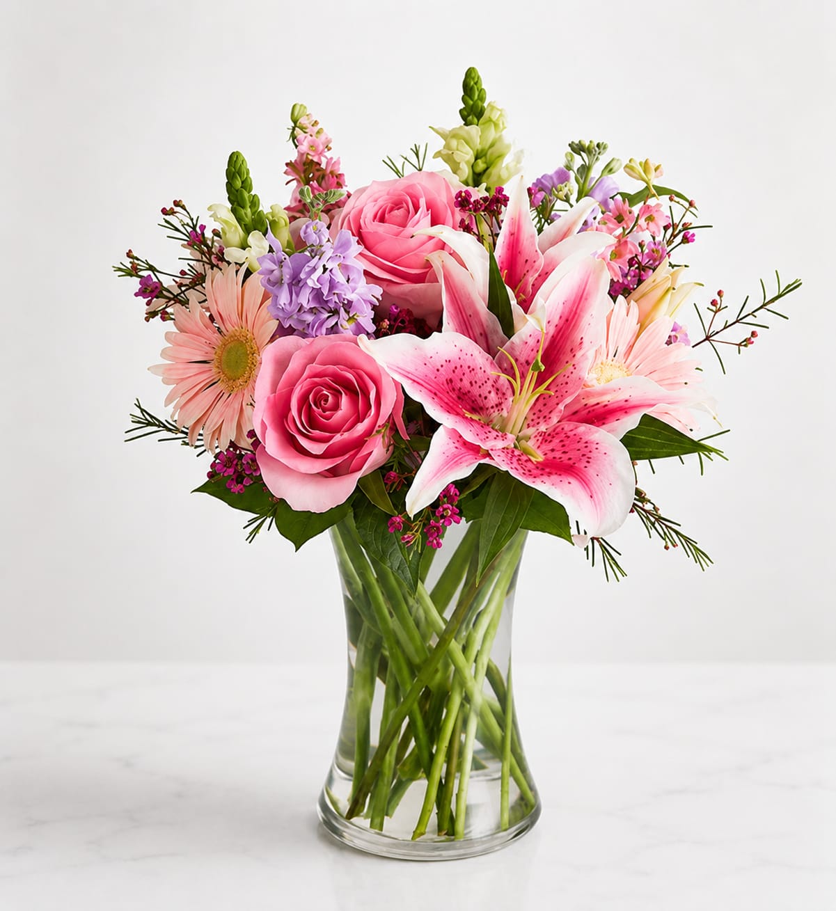 Blushing Garden Elegance™ - Soft, elegant, and full of charm, Blushing Garden Elegance™ features gorgeous pink roses, fragrant pink Stargazer lilies, delicate gerbera daisies, snapdragons, stock, waxflower, and premium seasonal blooms arranged with lush greenery in a clear glass vase. This graceful bouquet is perfect for birthdays, anniversaries, thank-you gifts, get well wishes, or simply brightening someone's day with timeless beauty.