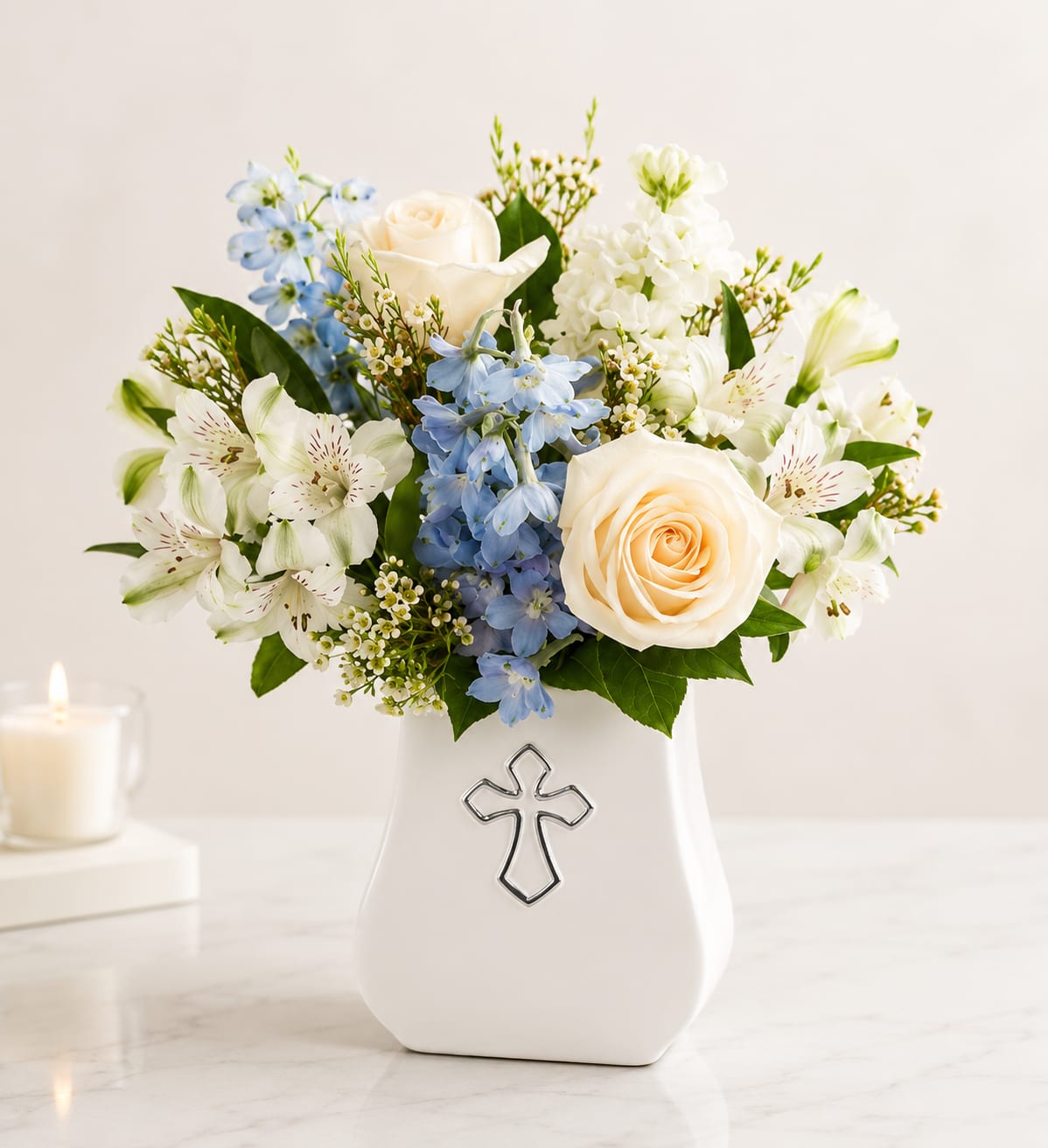 Heavenly Peace Bouquet - Offer comfort and heartfelt condolences with this elegant arrangement featuring white roses, white alstroemeria, delicate blue delphinium, fragrant white stock, and seasonal accent flowers beautifully arranged in a keepsake cross vase. A graceful expression of love, remembrance, and hope during life's most difficult moments.
