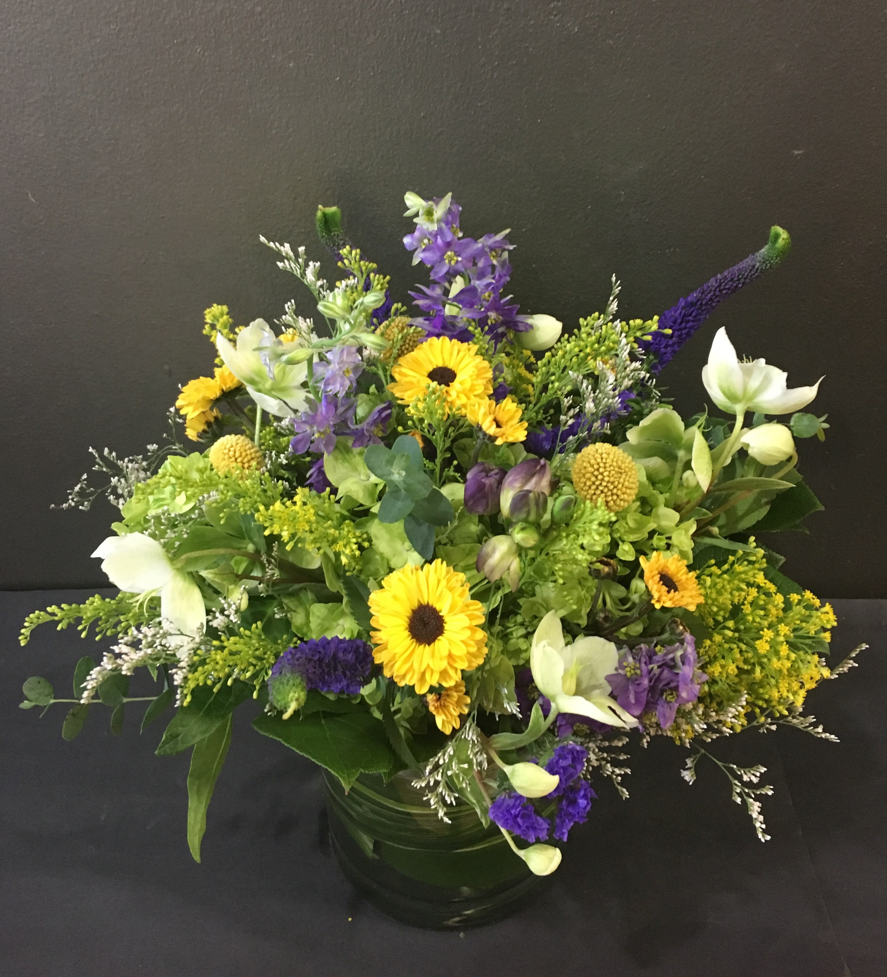 Low mixed arrangement of yellow and purple flowers in a round clear glass vase
