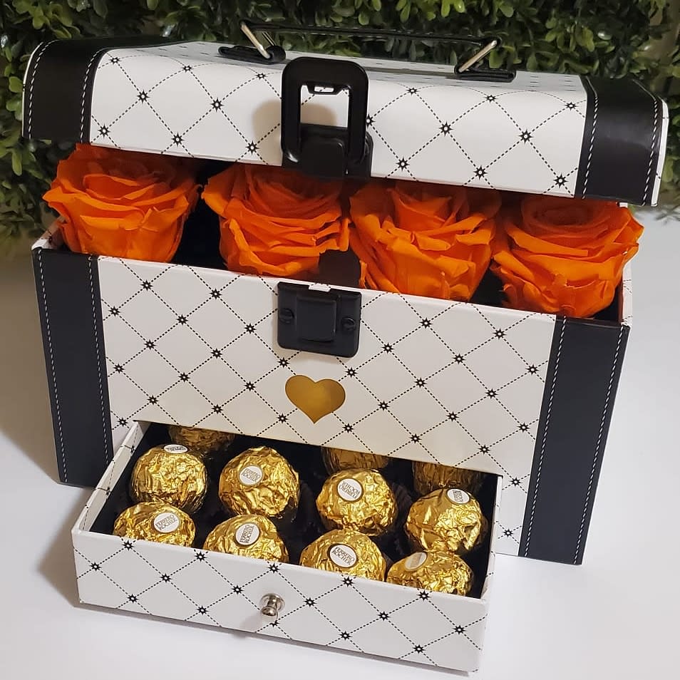 Orange roses in a decorative gift box above a drawer of gold-wrapped chocolates