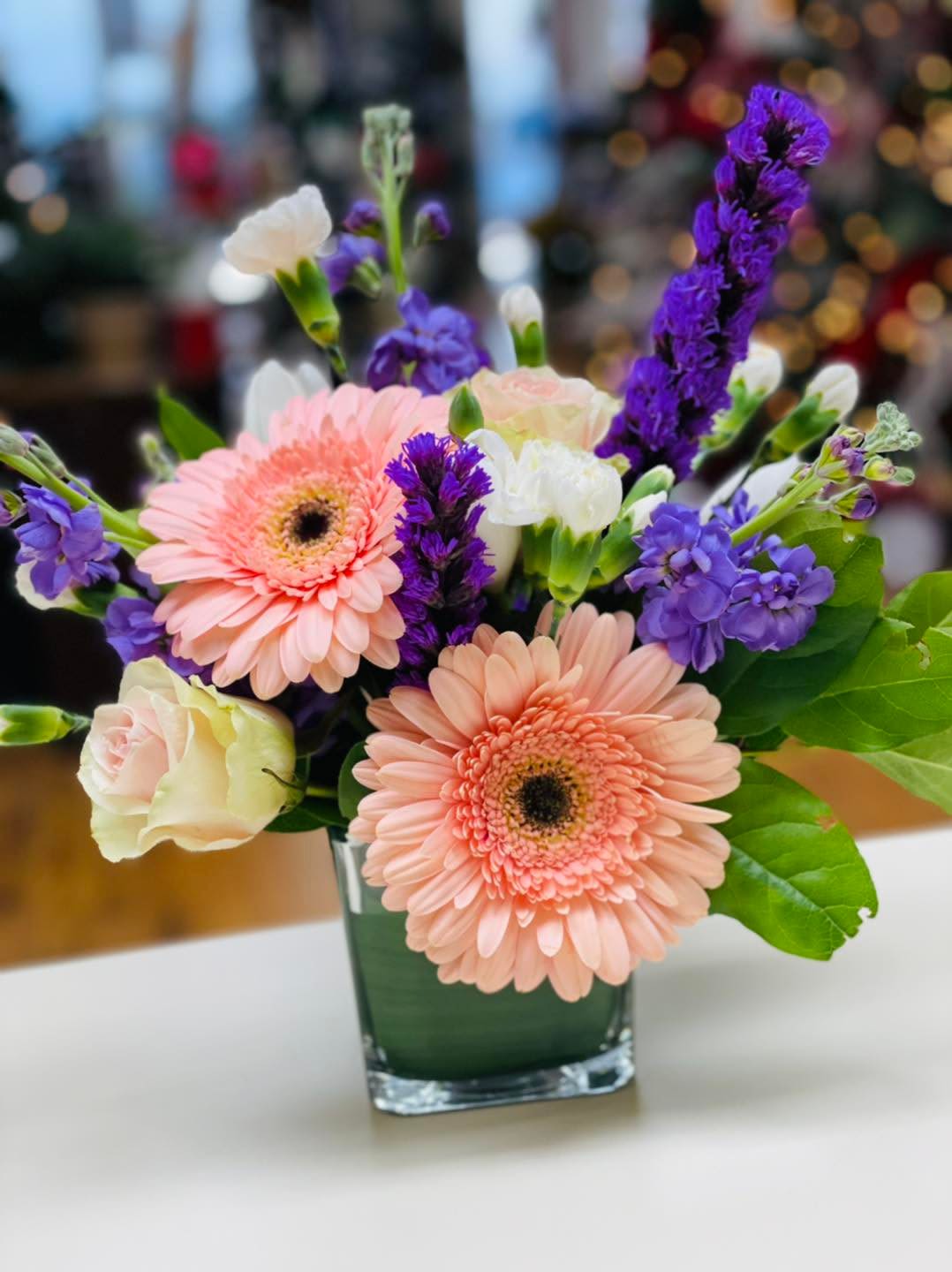 Pink gerbera daisies and purple flowers in a glass vase