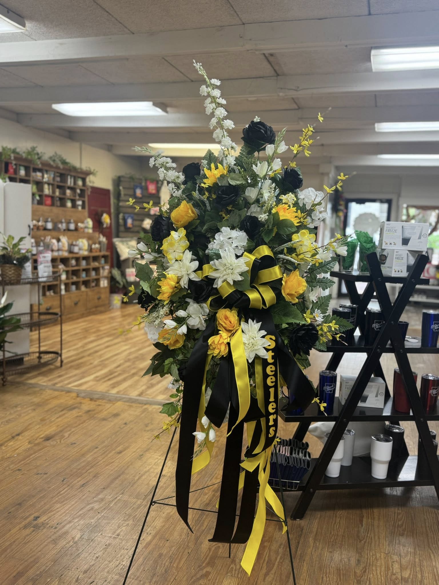 Tall black, white, and yellow funeral spray on an easel with ribbons