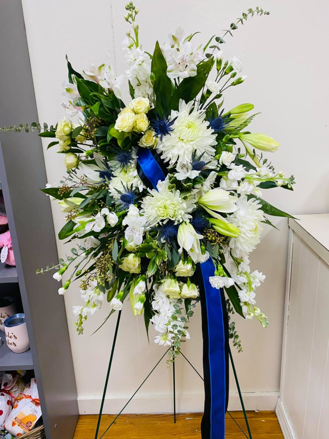 Large white floral standing spray with blue ribbon on an easel