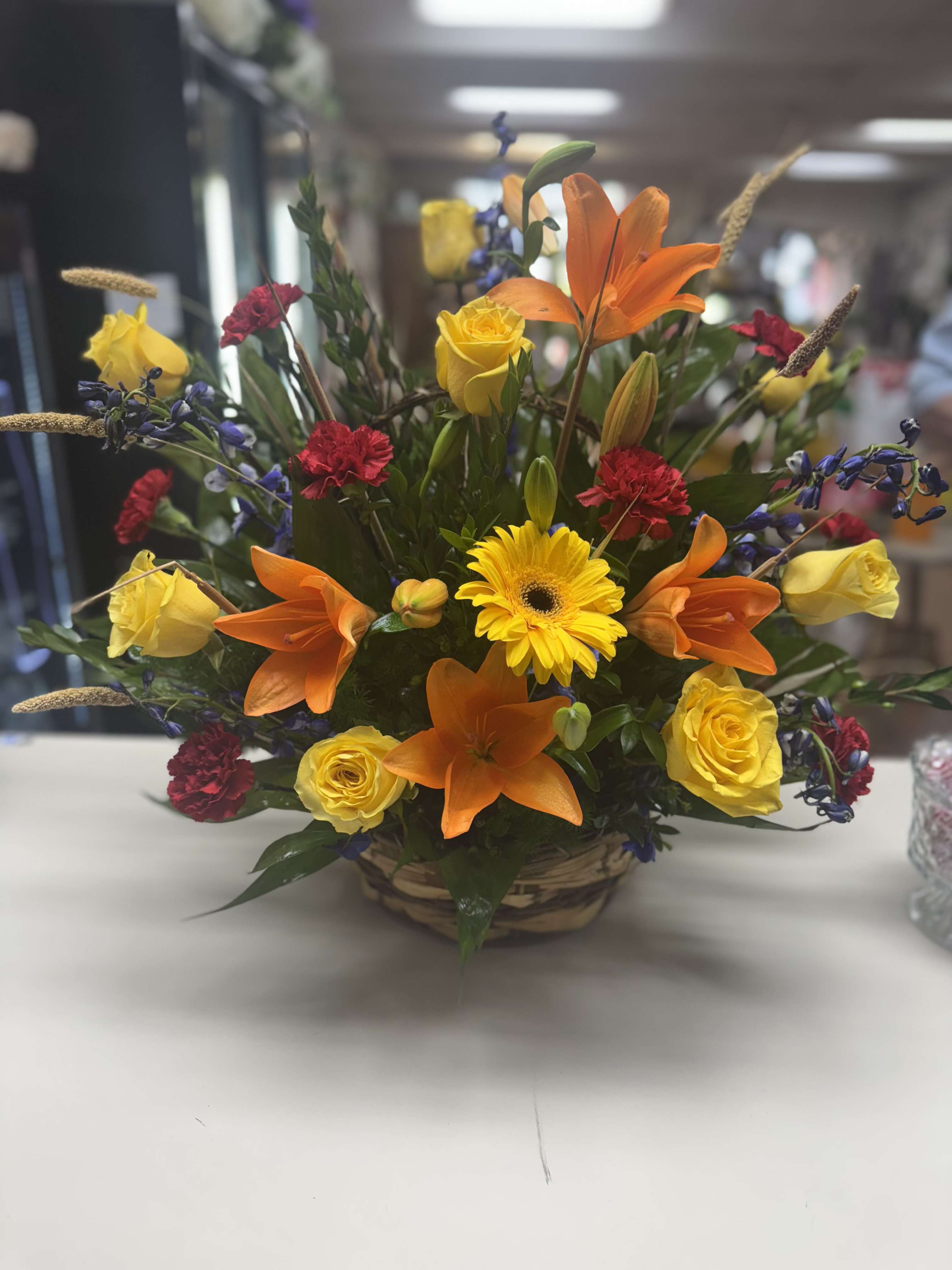 Mixed bouquet with orange lilies, yellow roses, and a yellow gerbera daisy in a basket