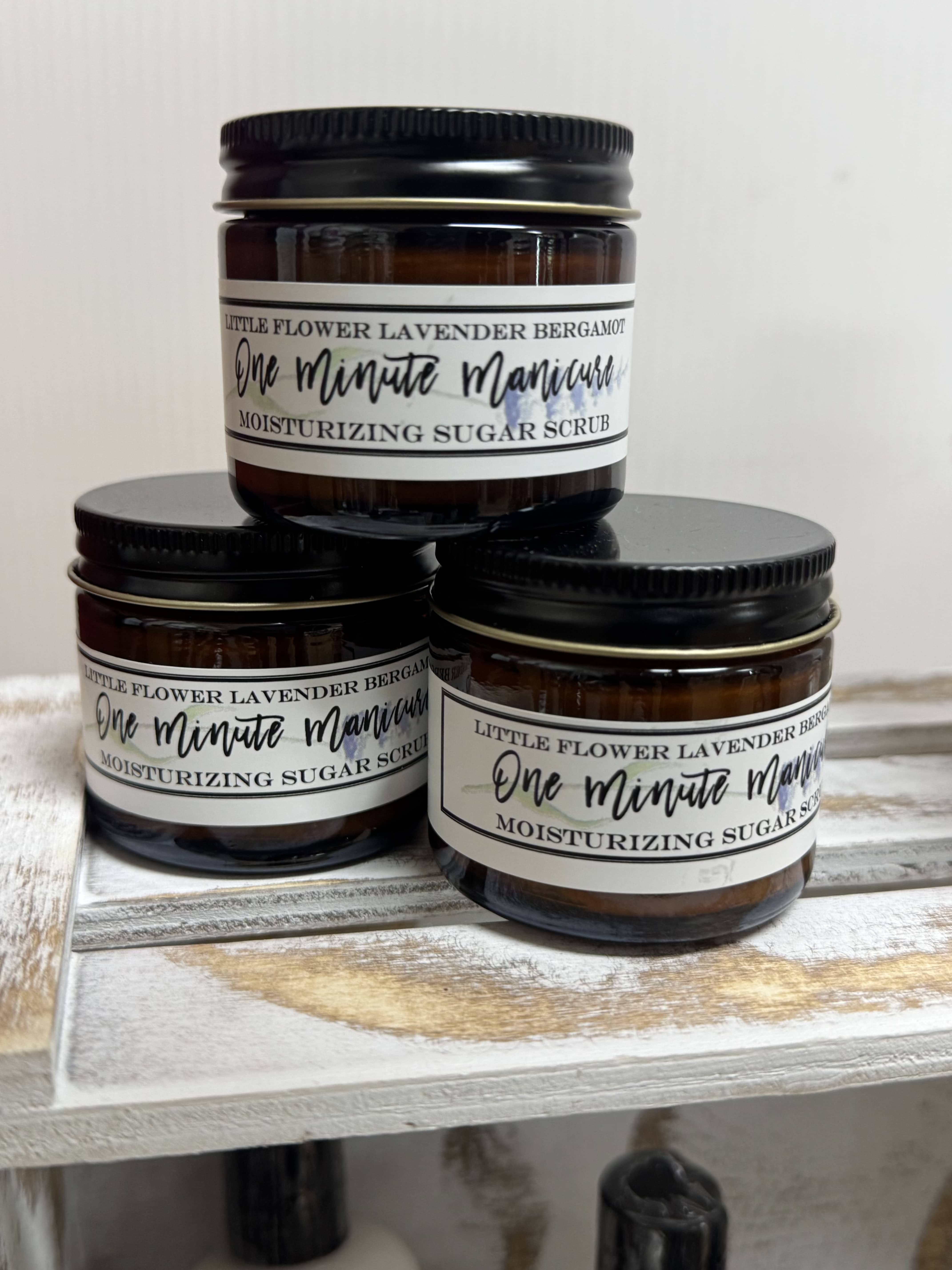 Three amber jars of lavender bergamot sugar scrub stacked on a wooden surface.