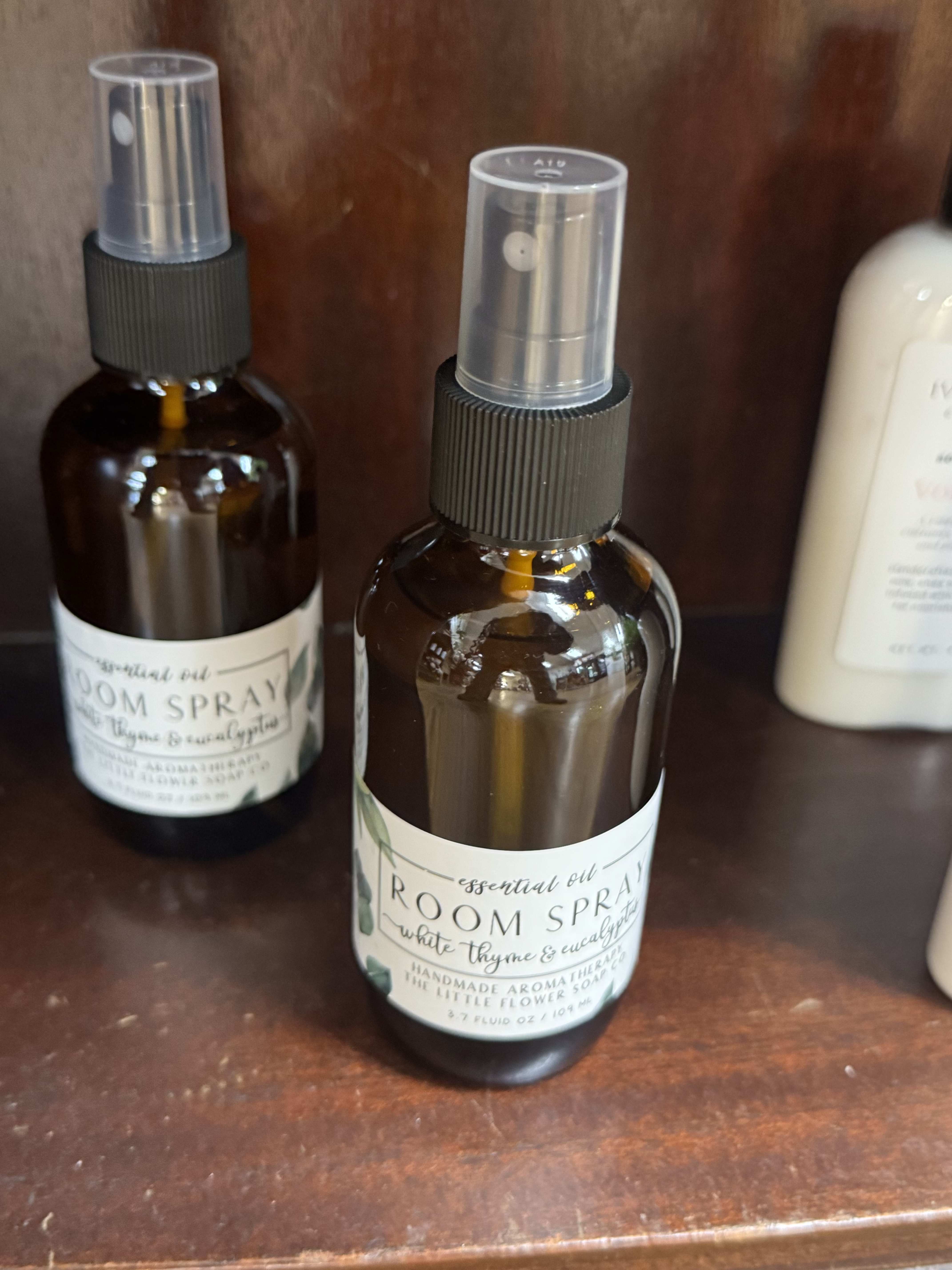 Two amber room spray bottles with clear caps sit on a wooden shelf.
