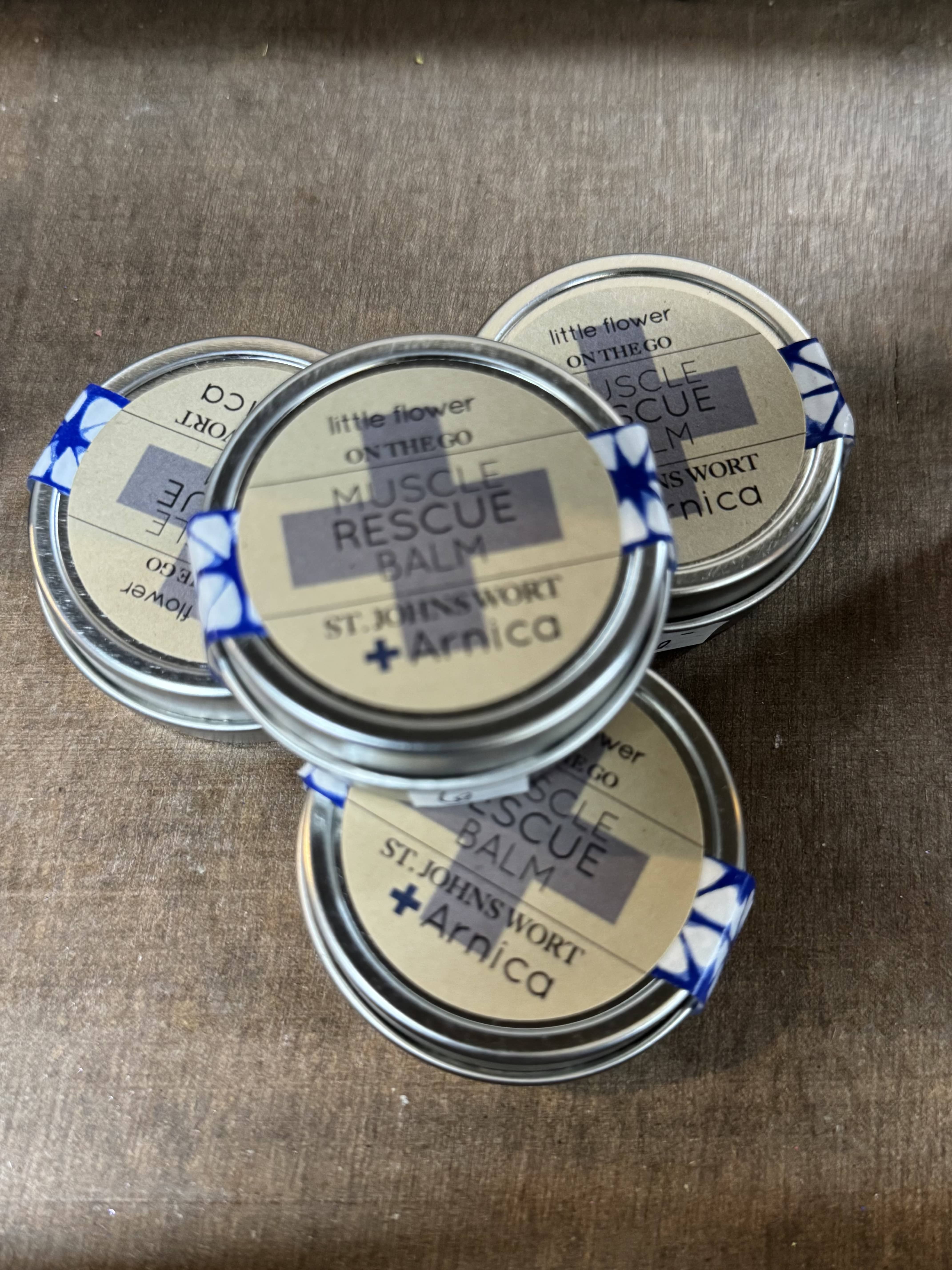 Four small tins of muscle rescue balm on a wooden surface