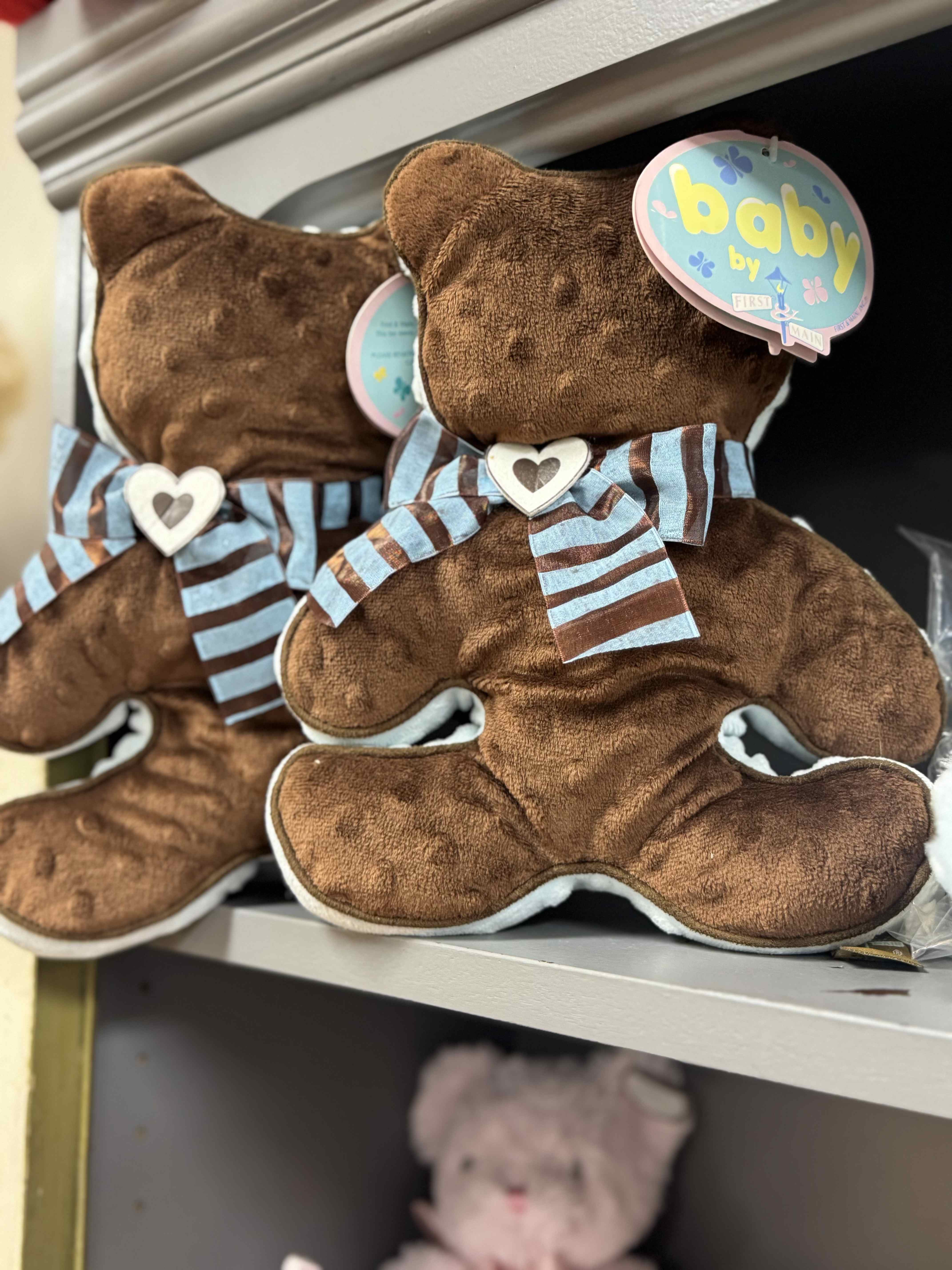 Two teddy bears with baby tags and striped bows on a shelf