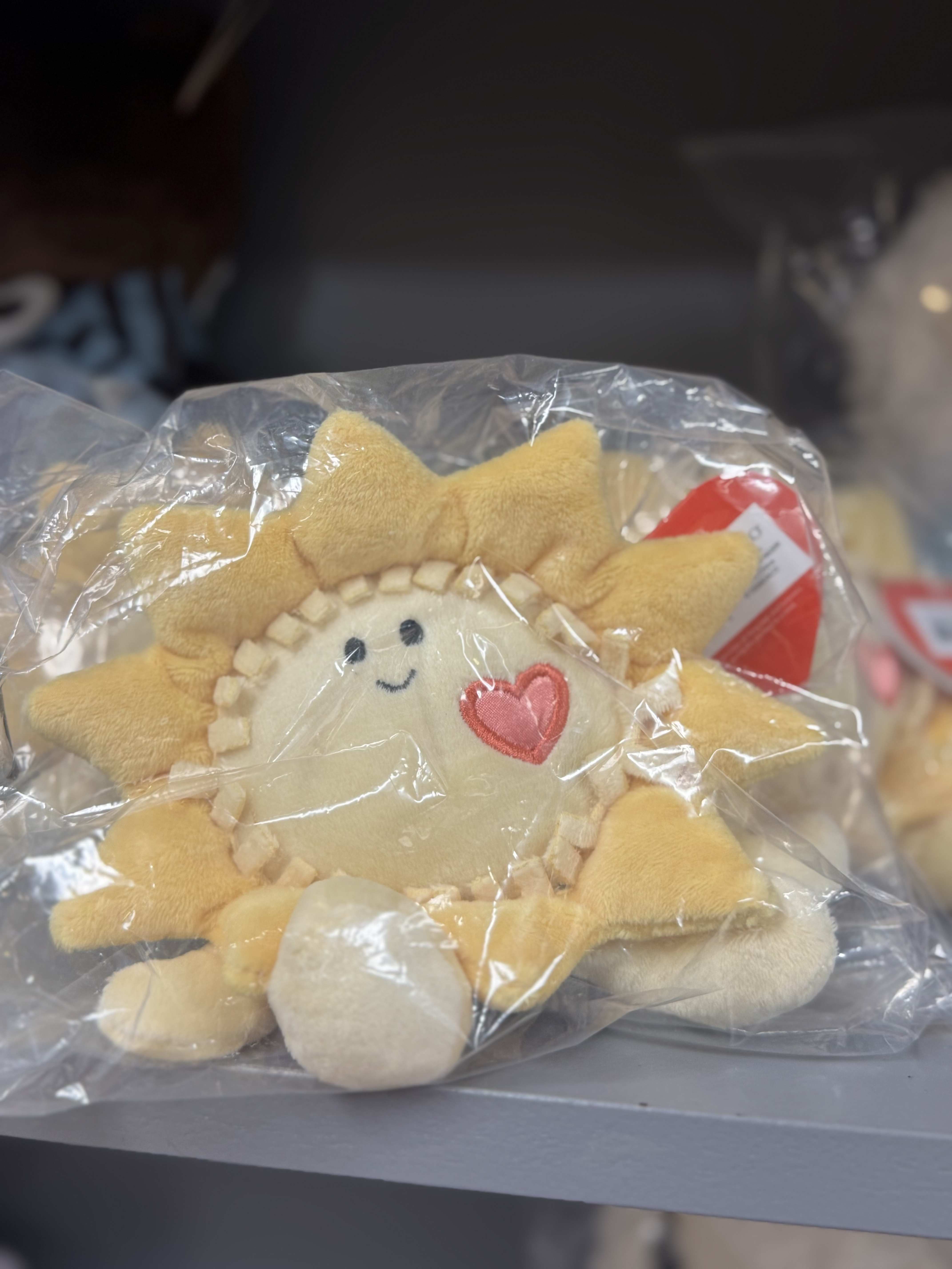 Plush sun-shaped toy in a clear plastic bag with a heart patch