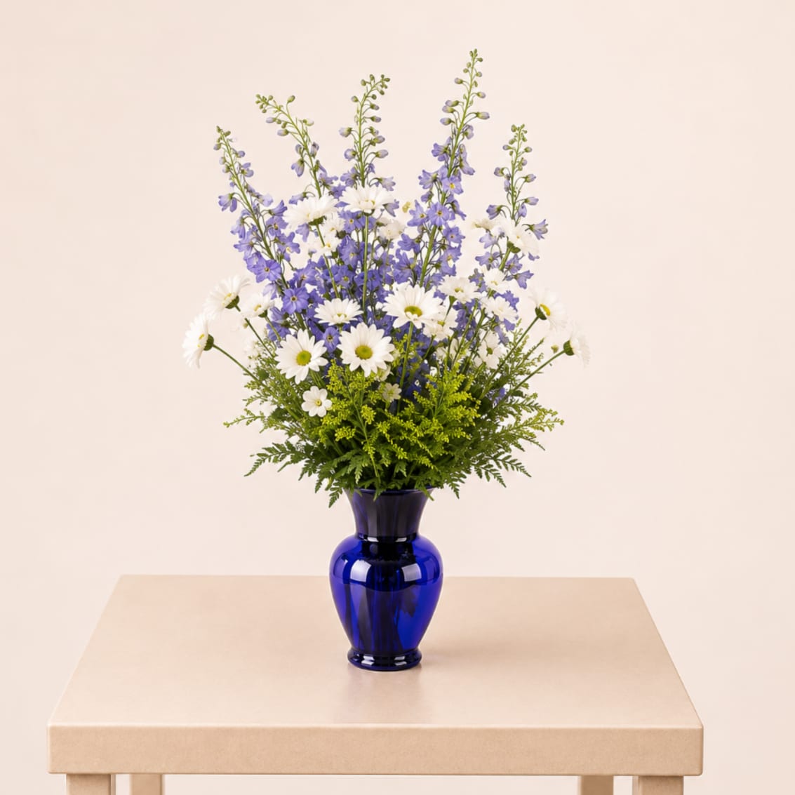 Blue Skies - A bright and airy flower arrangement featuring soft blue blooms and crisp white daisies, beautifully designed in a cobalt blue vase for a fresh, uplifting, and joyful look.  Each arrangement is Designer’s Choice, thoughtfully created with fresh seasonal blooms. Flower varieties and color tones may vary based on availability while preserving the overall style, palette, and quality.  Perfect for sympathy, get well wishes, Mother’s Day, thank you gestures, welcoming a new baby, thinking of you, or a cheerful birthday surprise.  Proudly handcrafted by Studio K Floral Boutique, offering flower delivery in Naples, Fort Myers Beach, Bonita Springs, Estero Fl. 
