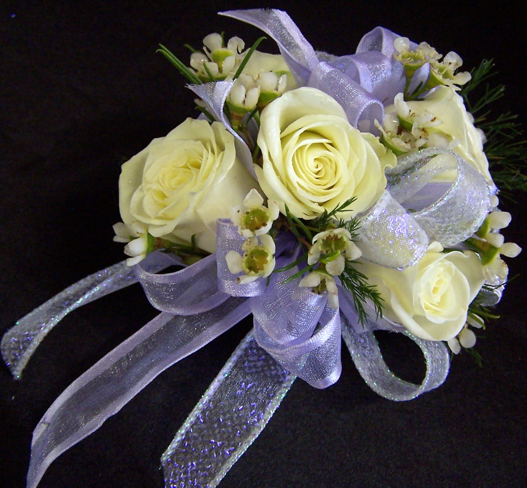 All White Wristlett Corsage - This corsage is made up of all white spray roses, white wax flowers and accented with white shear ribbon and white iridescent ribbon on a rhinestone bracelet.  *Please note upgrade price for added details. 