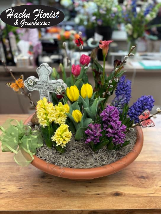 Mixed spring flowers in a shallow terracotta bowl with a decorative cross
