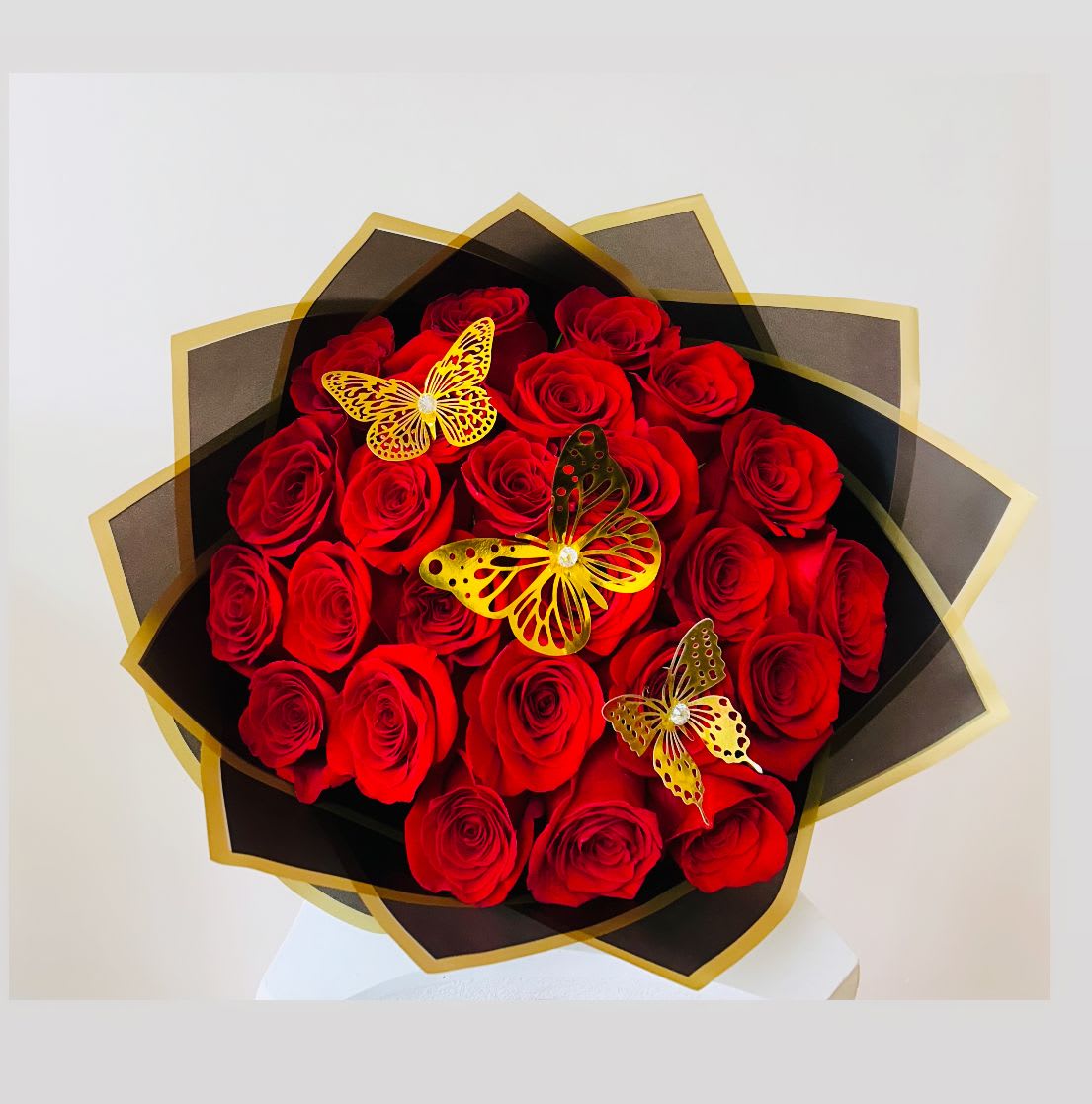 Bouquet of red roses wrapped in black and gold paper with butterfly decorations