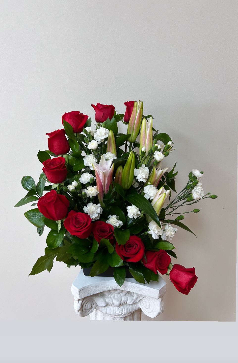 Red roses and white lilies arranged in a vase with small white filler flowers
