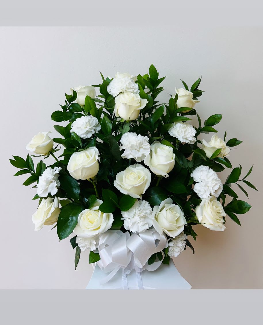 White roses and carnations arranged with a white ribbon bow