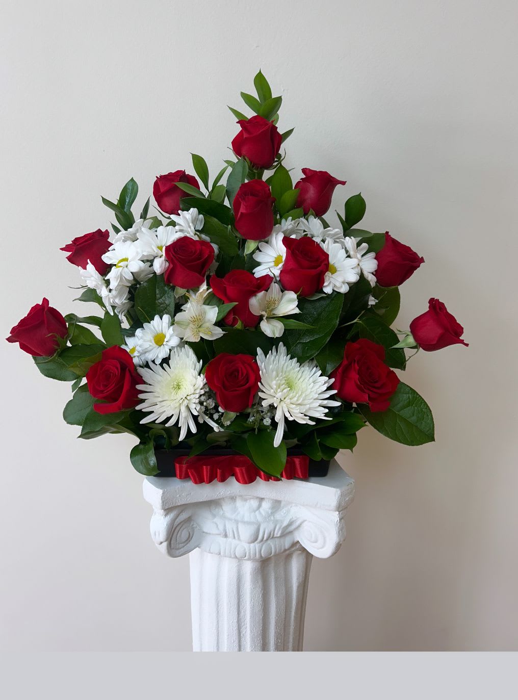 Red roses and white daisies arranged in a pedestal display