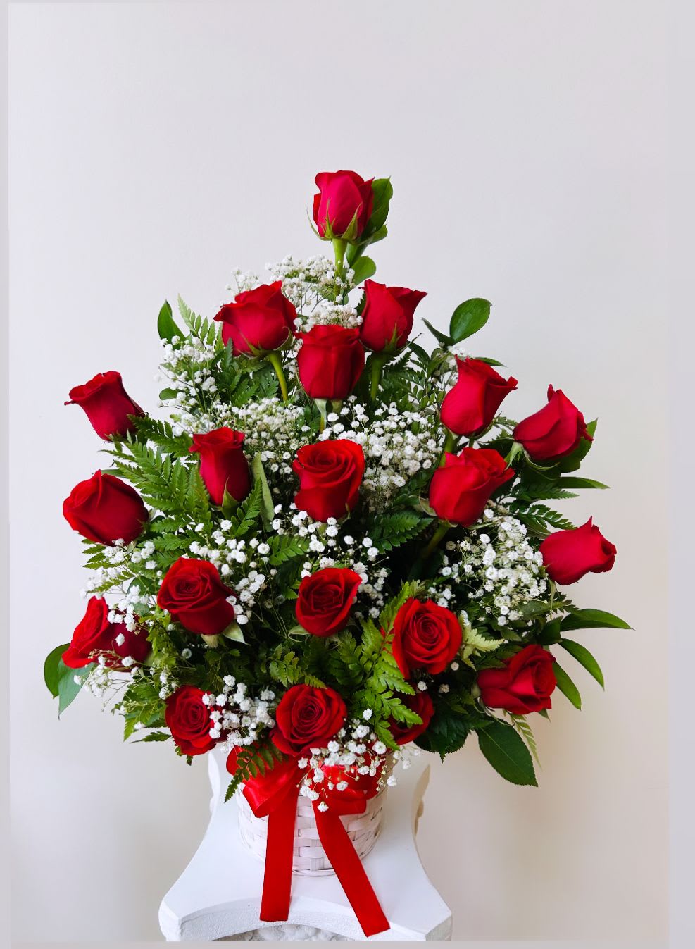 Red roses arranged in a white basket with baby's breath