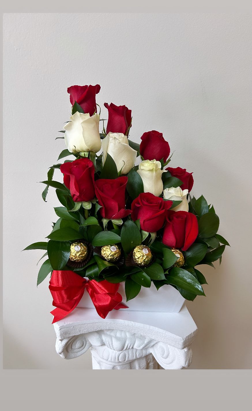 Red and white roses arranged with chocolates and a red ribbon