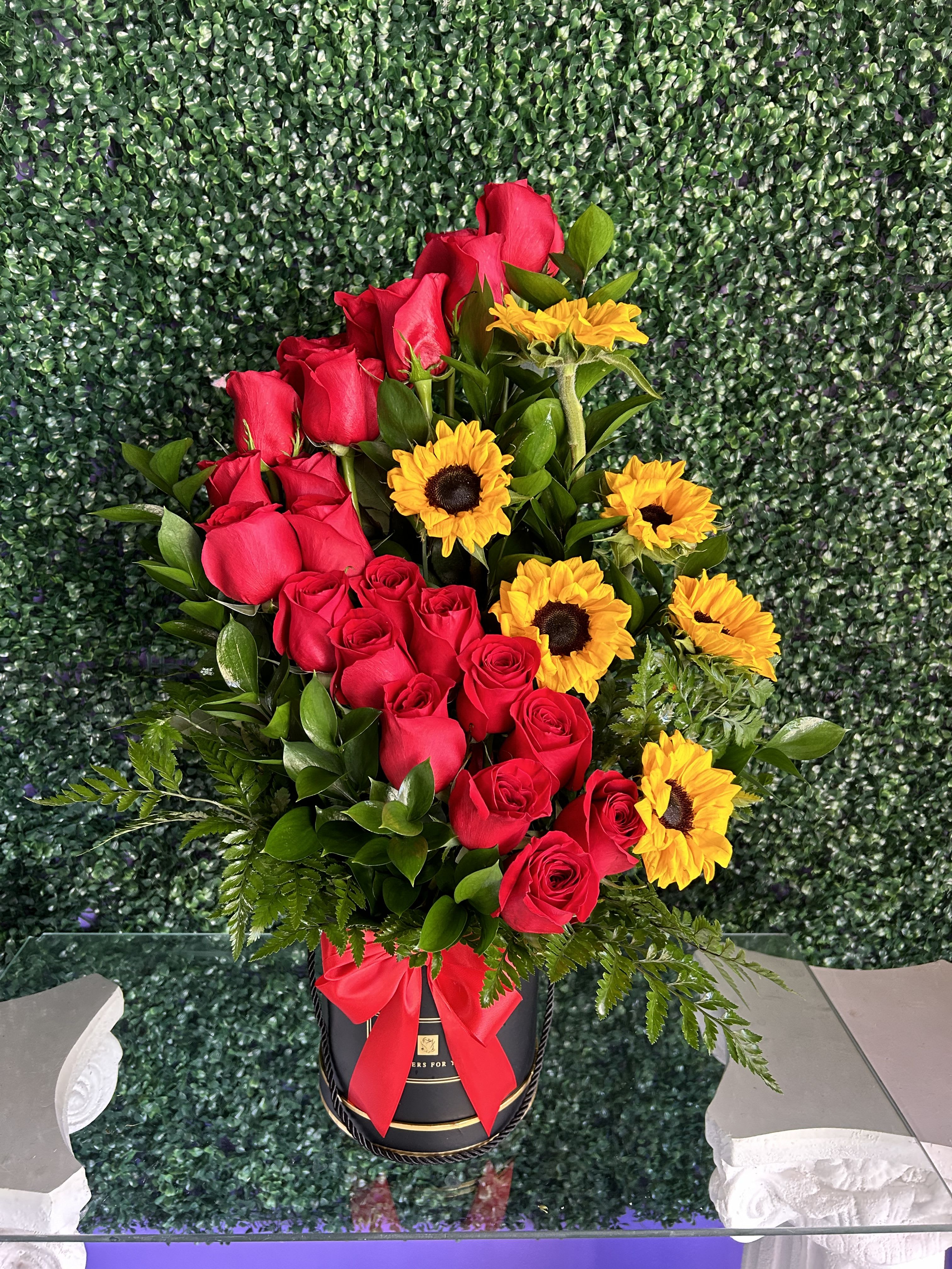 Red roses and yellow sunflowers in a black hatbox with a red ribbon