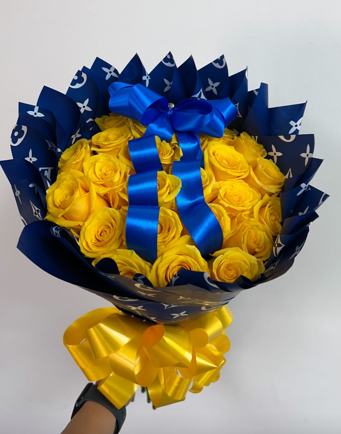 Bouquet of yellow roses wrapped in dark blue paper with a blue ribbon
