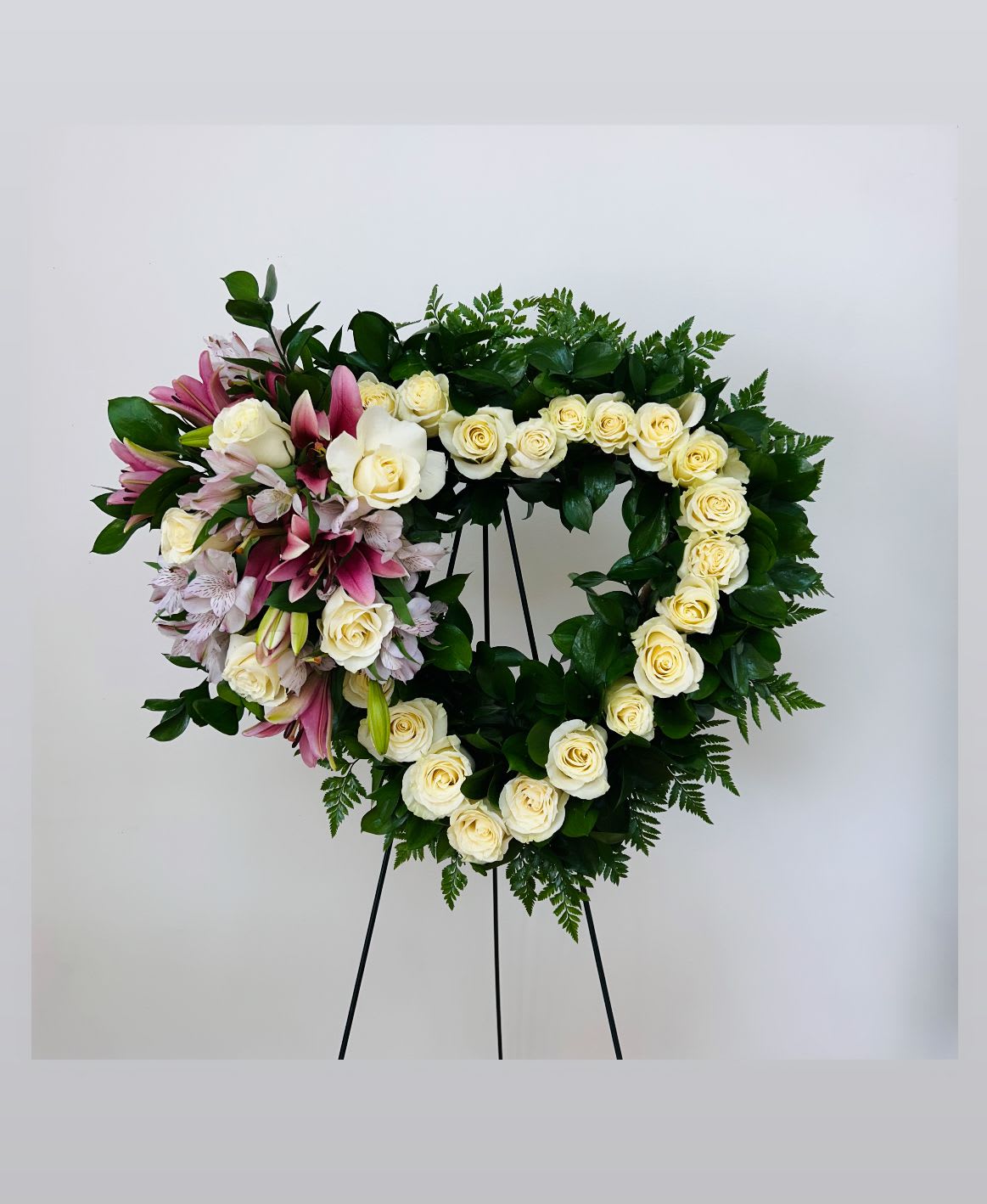 Heart-shaped floral wreath of white roses and pink lilies on a stand