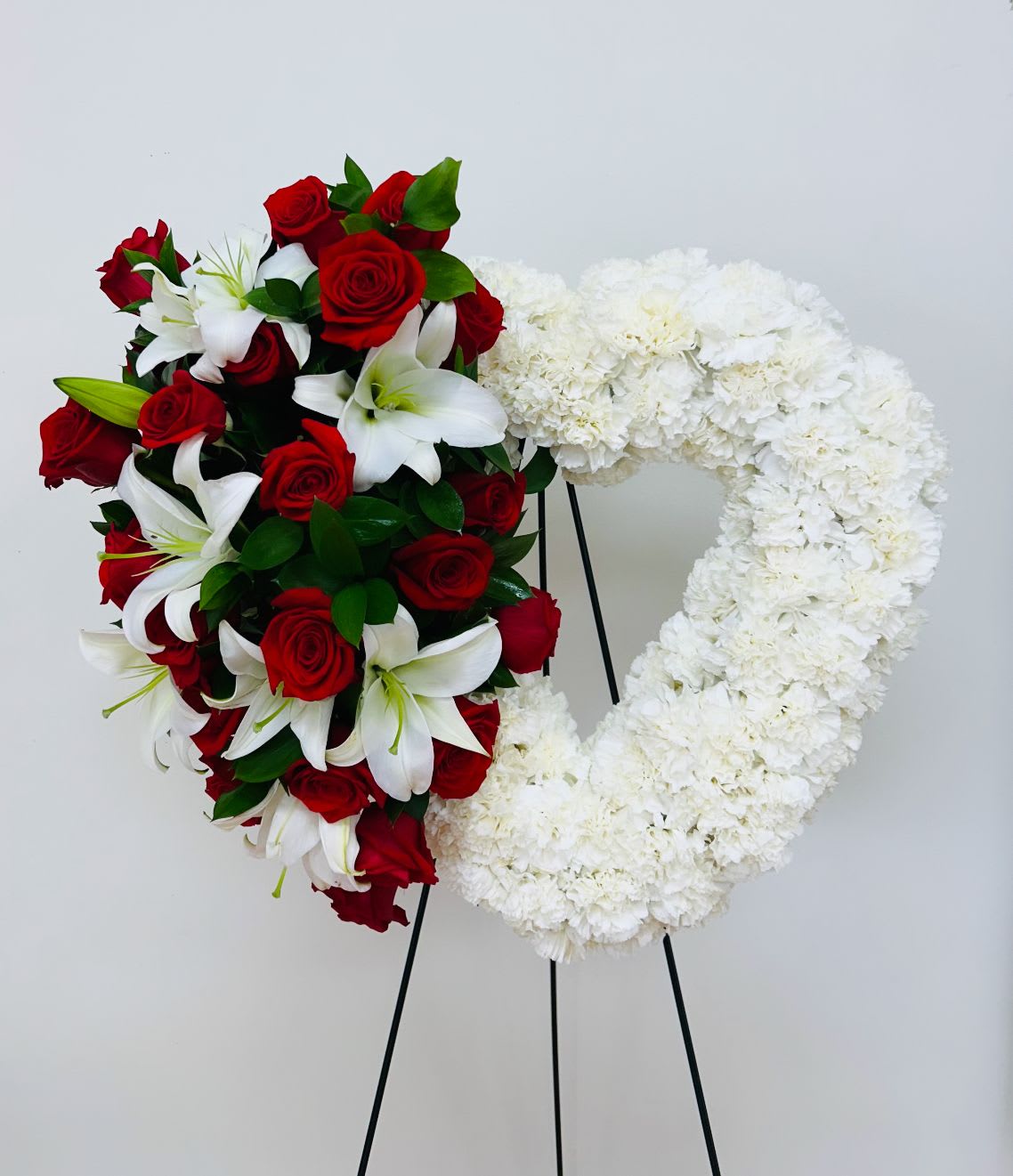 Heart-shaped floral wreath with red roses, white lilies, and white flowers on a stand