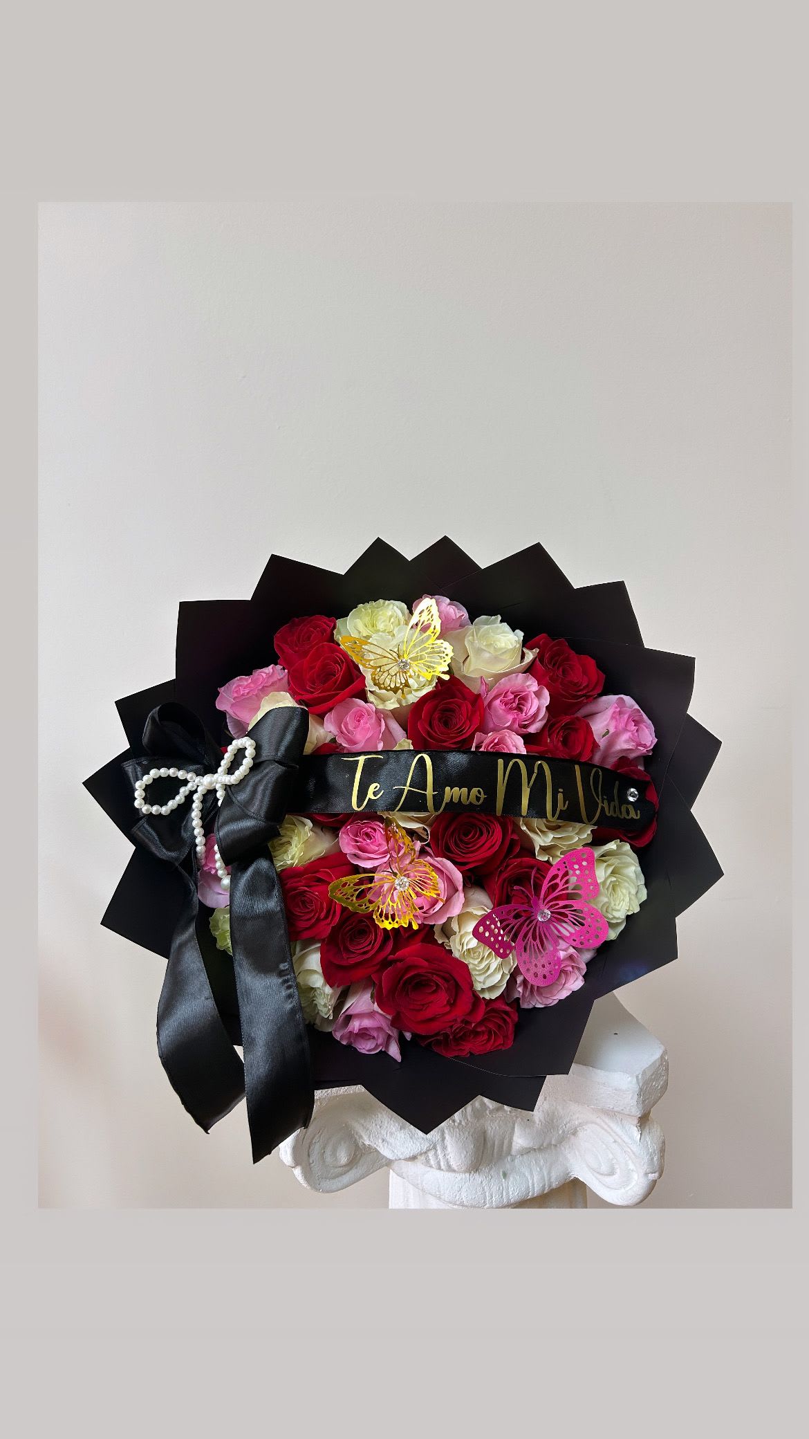 Bouquet of red, pink, and white roses with black ribbon and butterfly accents