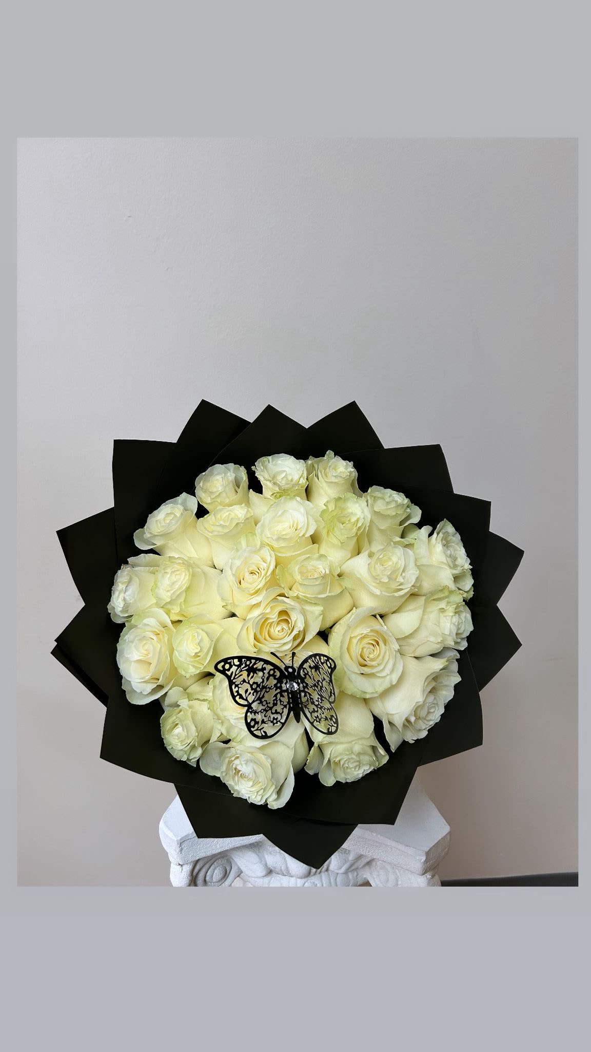 Bouquet of white roses wrapped in black paper with a butterfly decoration