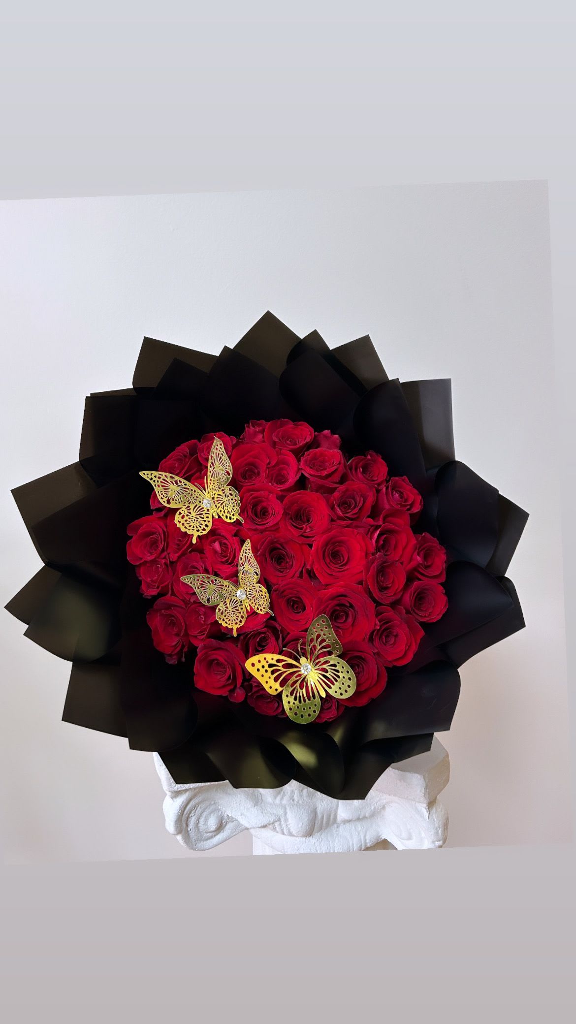 Bouquet of red roses wrapped in black paper with gold butterfly accents