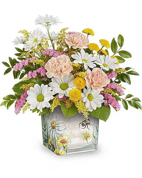 Honey Kissed Bouquet - Their heart will buzz like a busy bee when this enchanting floral gift arrives, featuring serene blooms in a keepsake glass cube adorned with delightful vintage garden imagery.  This bouquet showcases a delightful mix of peach carnations, yellow button spray chrysanthemums, white daisy spray chrysanthemums, pink sinuata statice, all beautifully arranged with solidago, huckleberry, lemon leaf for added texture. This bouquet is presented in the charming Floral Buzz cube.  Orientation : All-Around