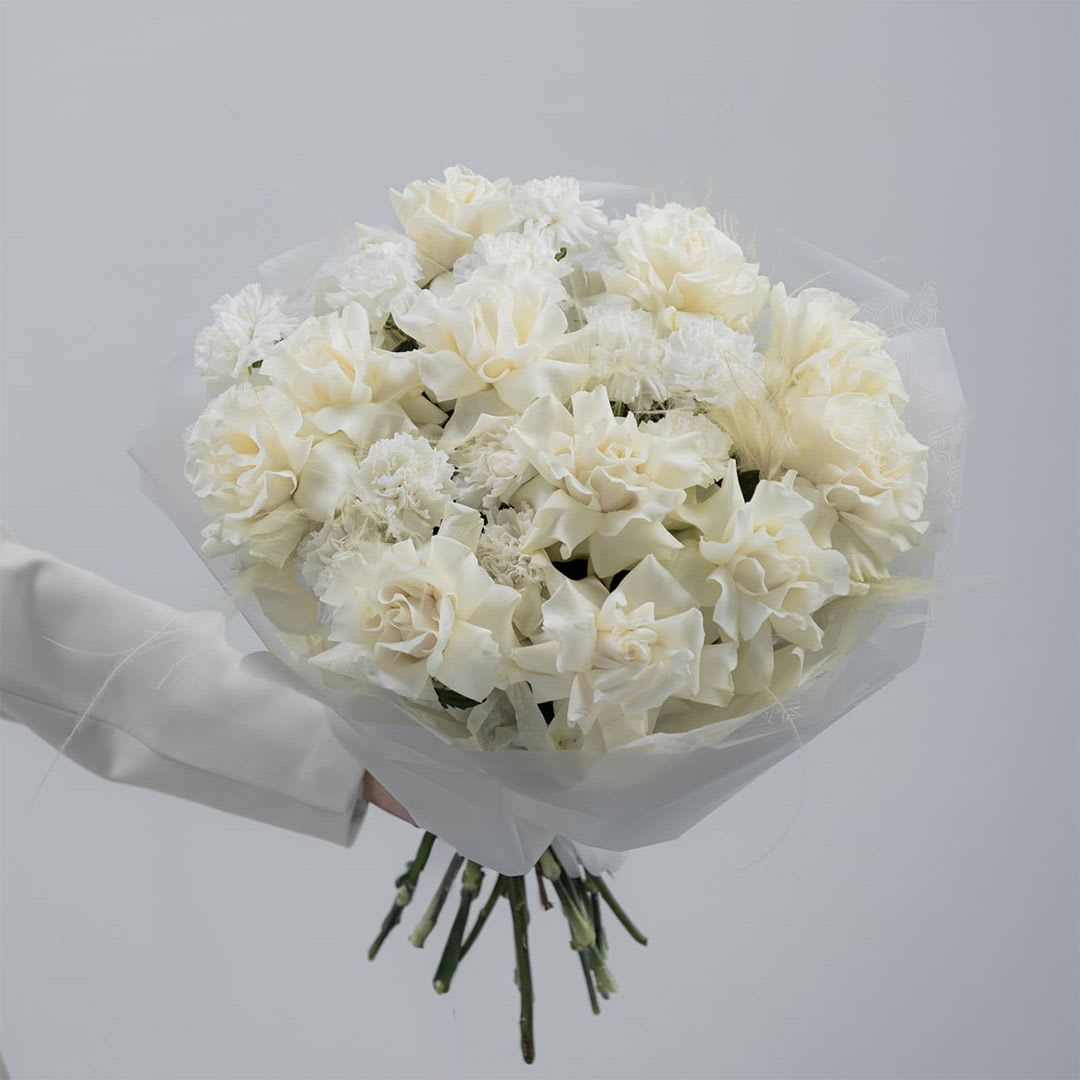     Pearl Bloom - A refined bouquet of white roses and white carnations wrapped in elegant white paper. Clean, graceful, and timeless, this monochromatic design offers a sophisticated expression of beauty and elegance for any meaningful occasion. Custom greeting card included.
