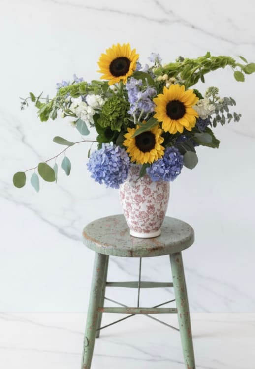 Summer Heritage  - Celebrate the beauty of a New England Summer with this arrangement that captures the warmth of a sunny day. Overflowing with blue hydrangeas, cheerful sunflowers and delicate greenery this piece is designed in a keepsake stoneware vase with a soft red toile pattern - a gift for the recipient to use again and again.  Approx 28" tall  housewarming, thank-you, Summer anniversary, 