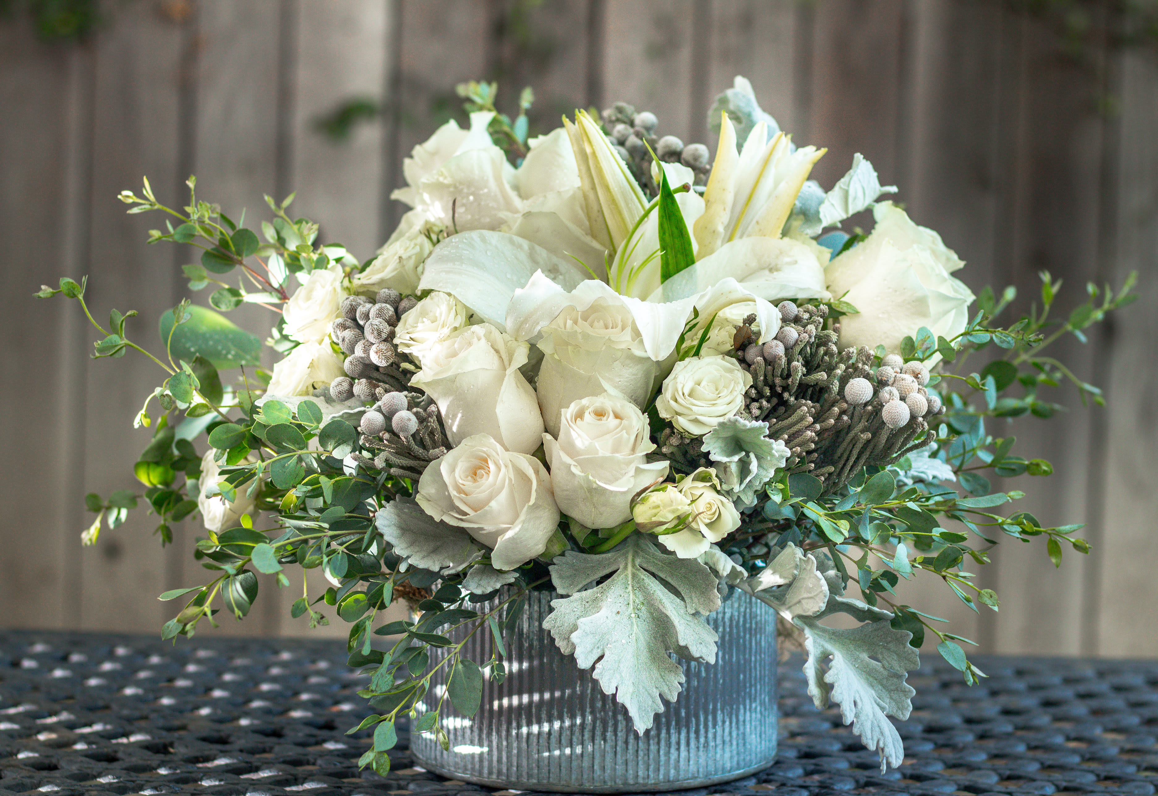 White roses and lilies arranged in a ribbed silver vase