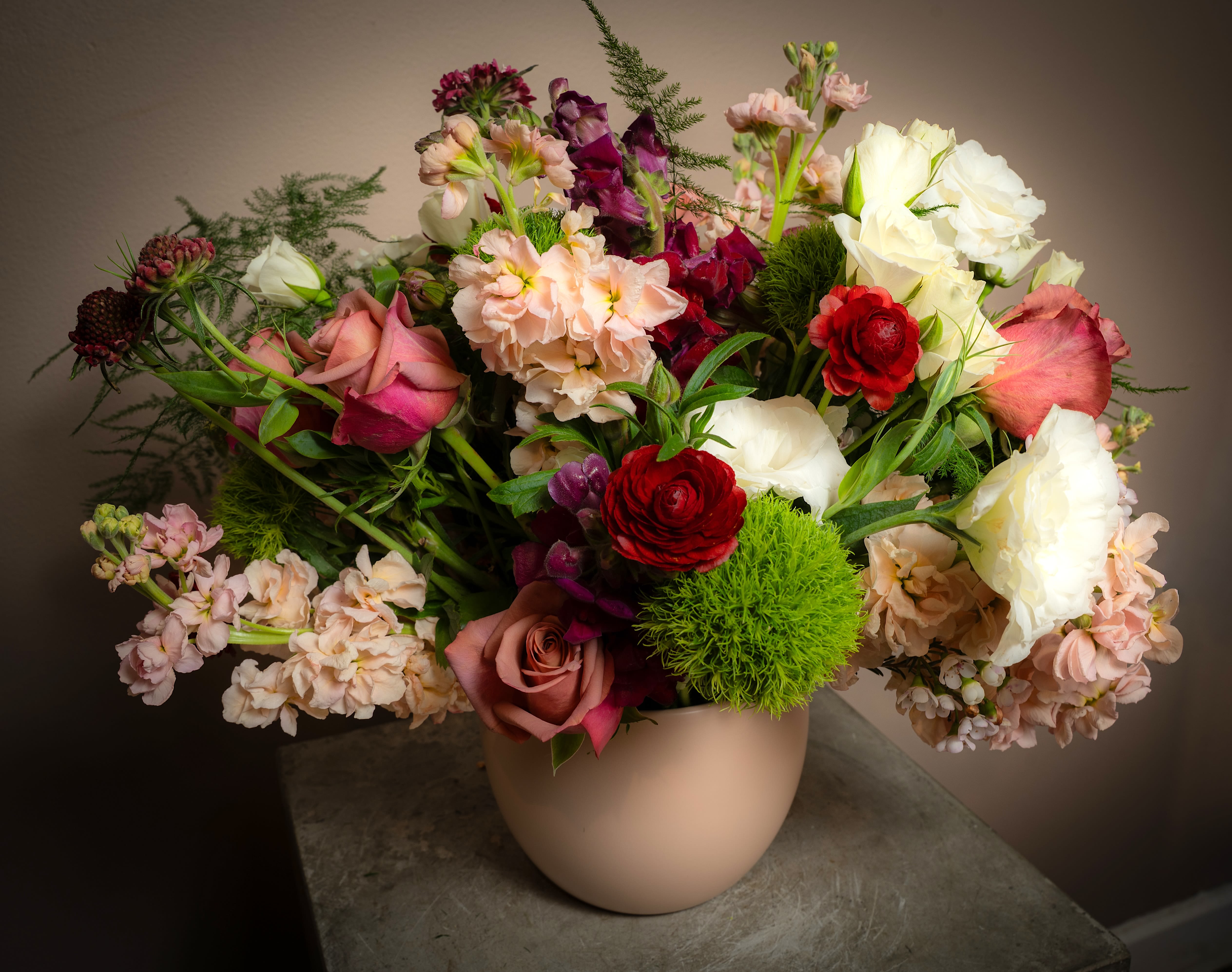 Mixed bouquet of roses, ranunculus, and stock in a beige vase