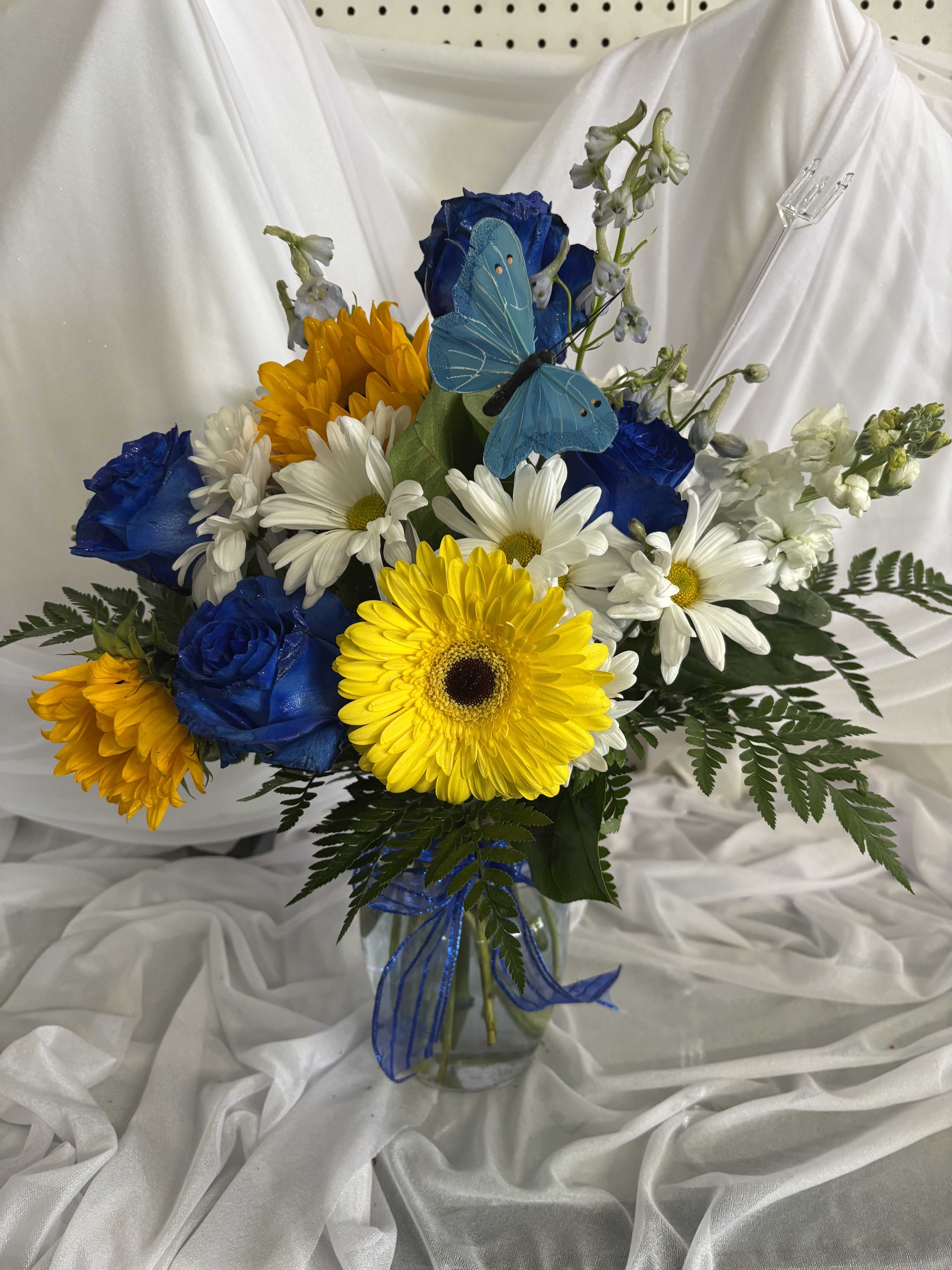 Bouquet of blue roses, white daisies, and yellow gerbera daisies in a glass vase