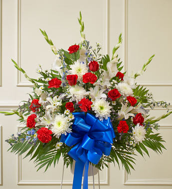 Red White And Blue Sympathy floor Basket - Convey your deepest condolences for a beloved veteran with this touching tribute. Our florists arrange beautiful red, white and blue flowers such as roses, hybrid lilies, cremones, delphiniums, carnations and more Traditionally sent by family, friends or business associates Sent directly to the funeral home Due to the sensitivity of the occasion, our florists use only the freshest flowers available, so colors and varieties may vary Arrangement measures approximately 32"H x 36"L    *please note: The picture features the bouquet on a stand. However, due to special circumstances, we are currently unable to get the stands for these containers. The arrangement can be placed on a table or the floor, but a stand will no be included. Thank you for your patience and understanding.*