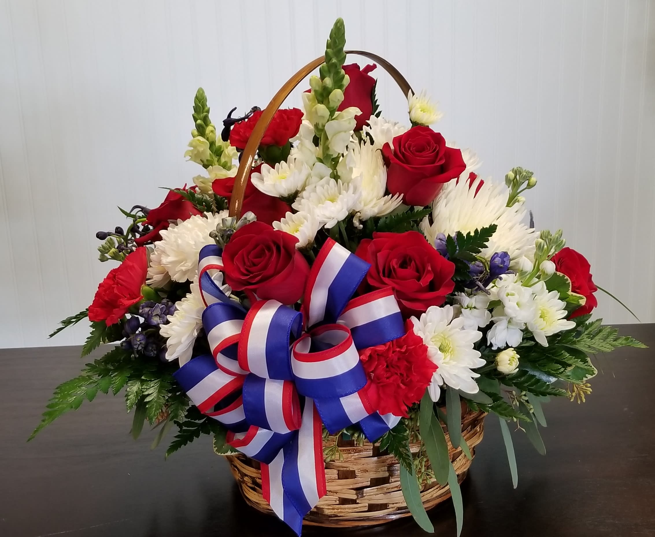 Basket arrangement of red roses and white daisies with a red-white-blue ribbon
