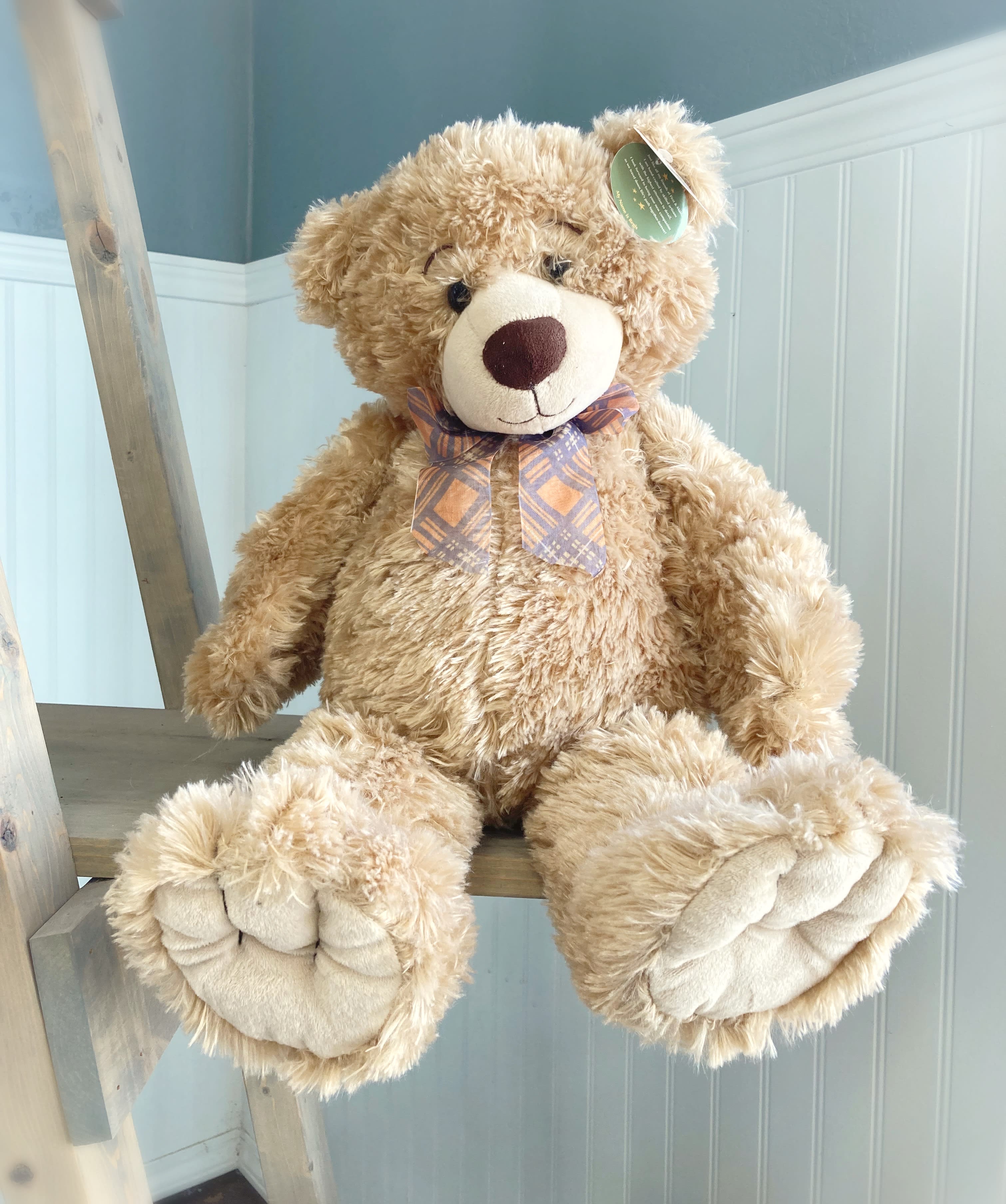 Large plush teddy bear with a plaid bow sitting on a wooden ladder