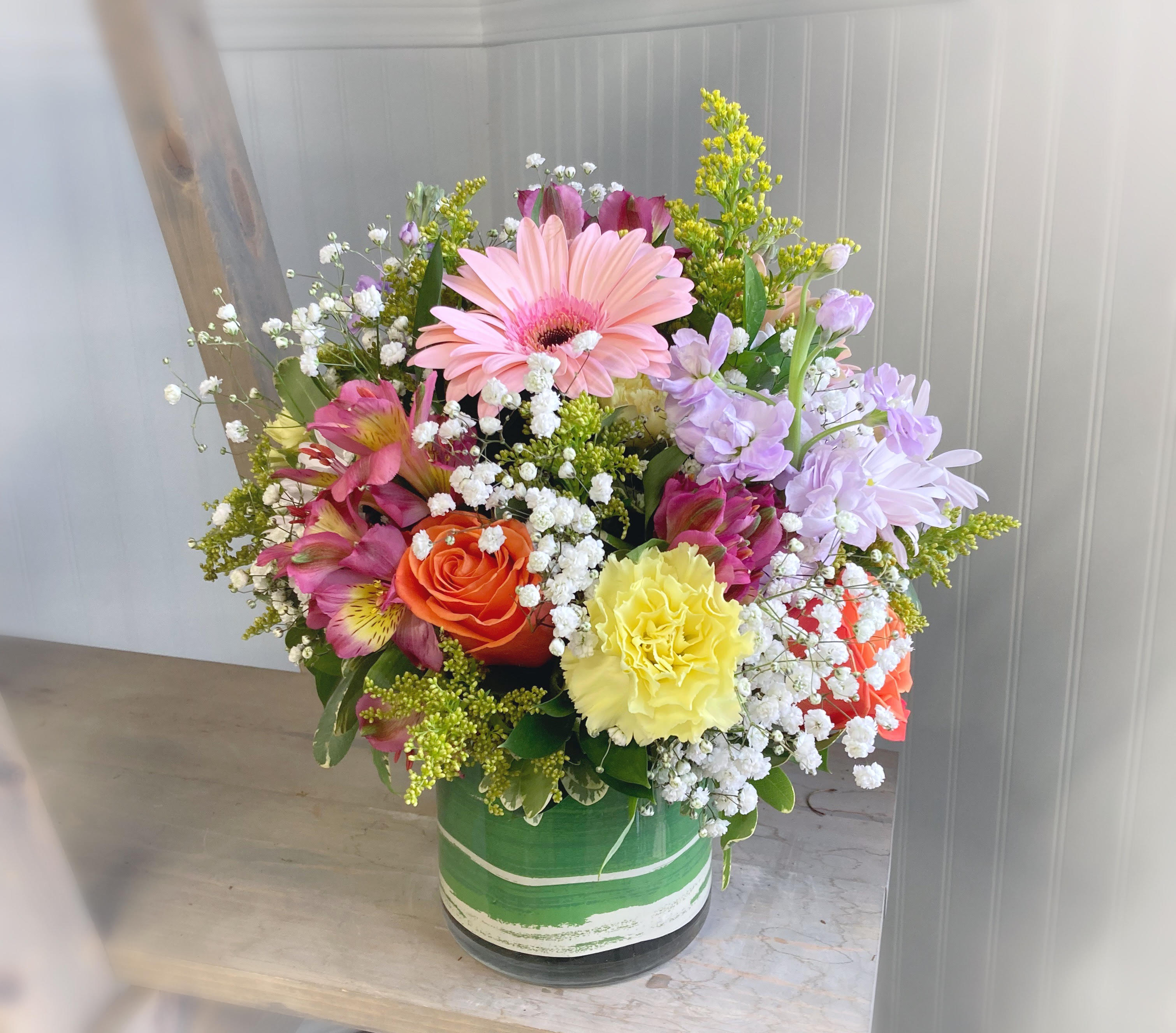 Mixed bouquet with pink gerbera, roses, carnations, and lavender blooms in a green vase