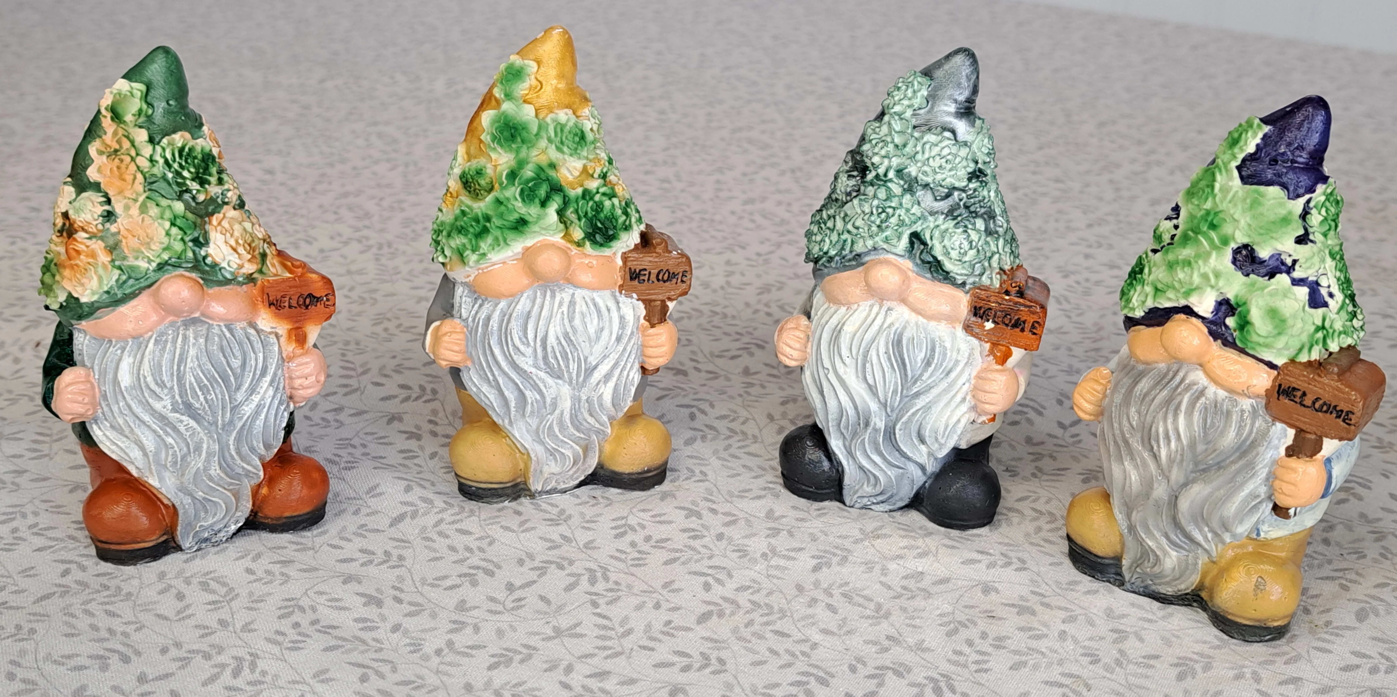 Set of four garden gnome figurines with flower-textured hats holding welcome signs