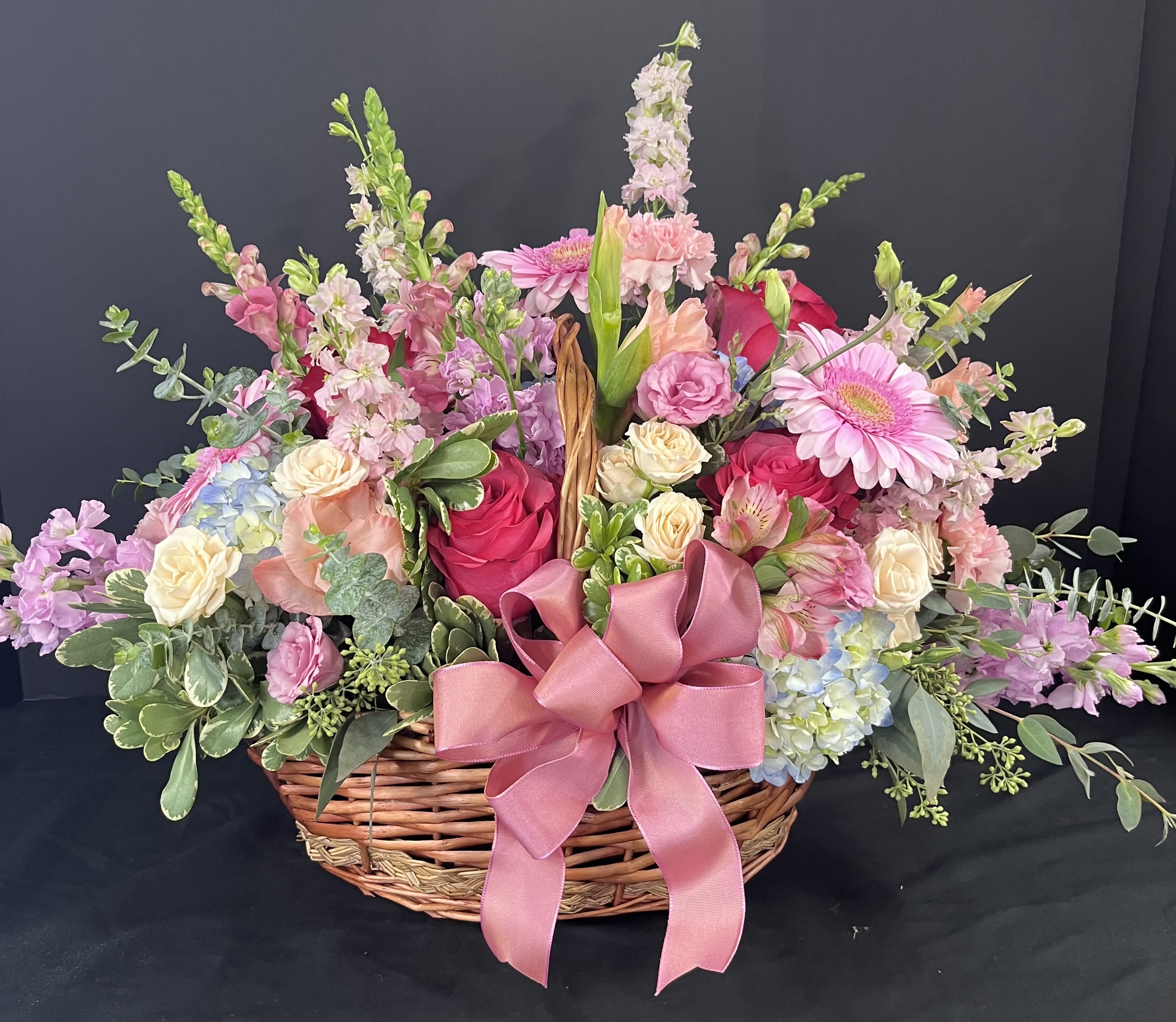 Basket arrangement of pink and cream flowers with a large pink ribbon